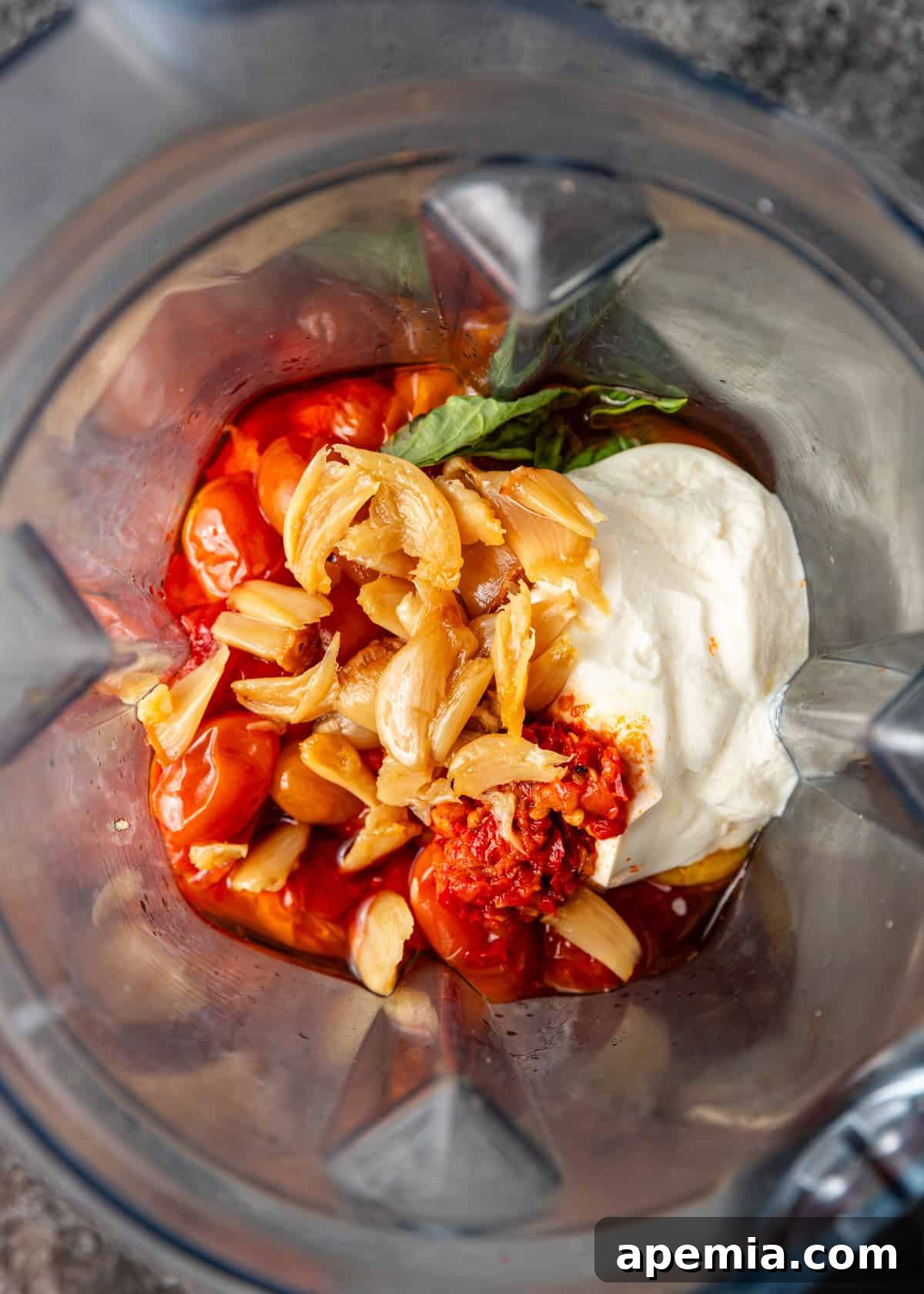Overhead process shot: ricotta cheese and garlic added to tomato confit mixture in blender, ready for blending