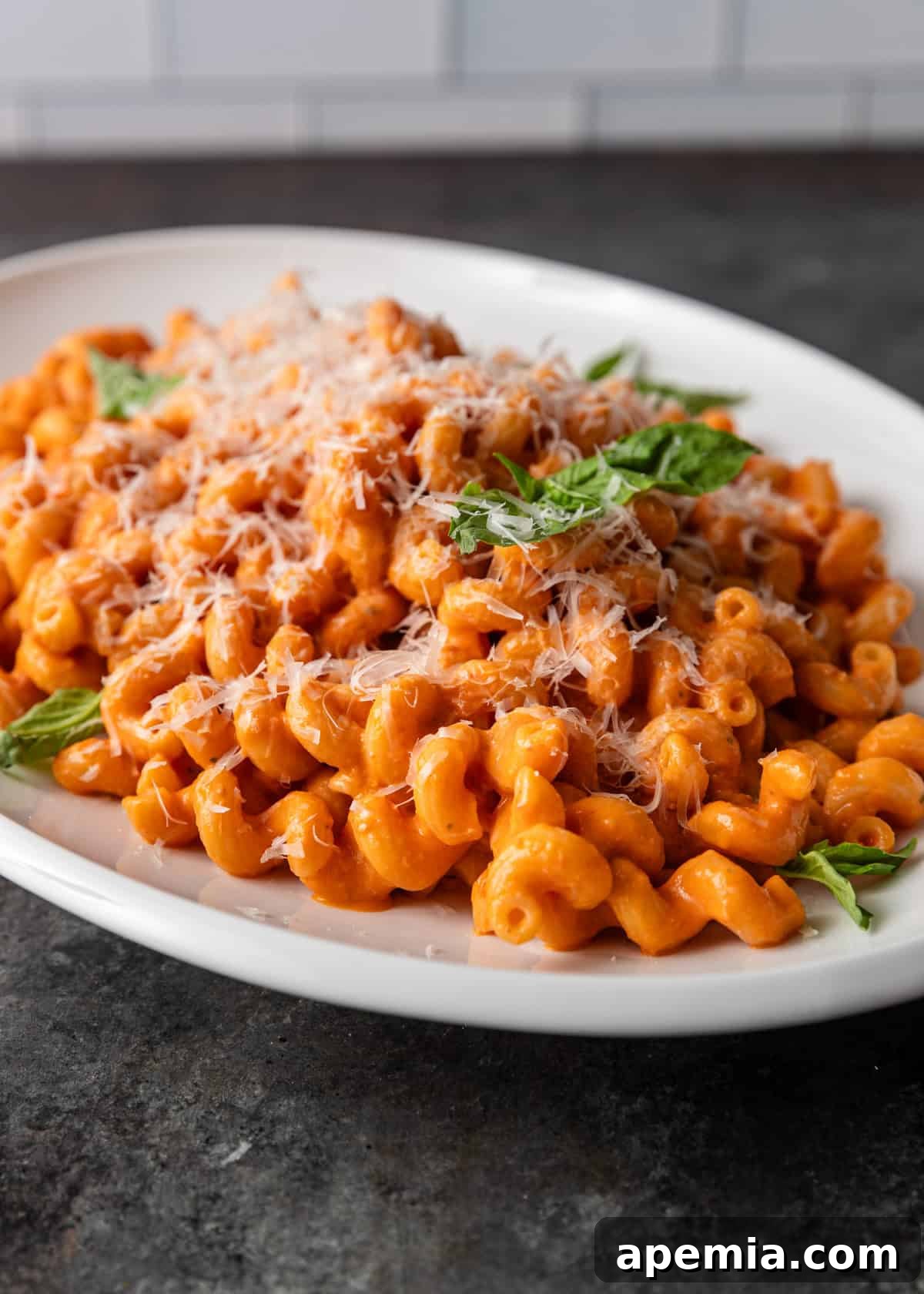 Close-up of tomato confit pasta with generous amounts of parmesan and fresh basil as garnish