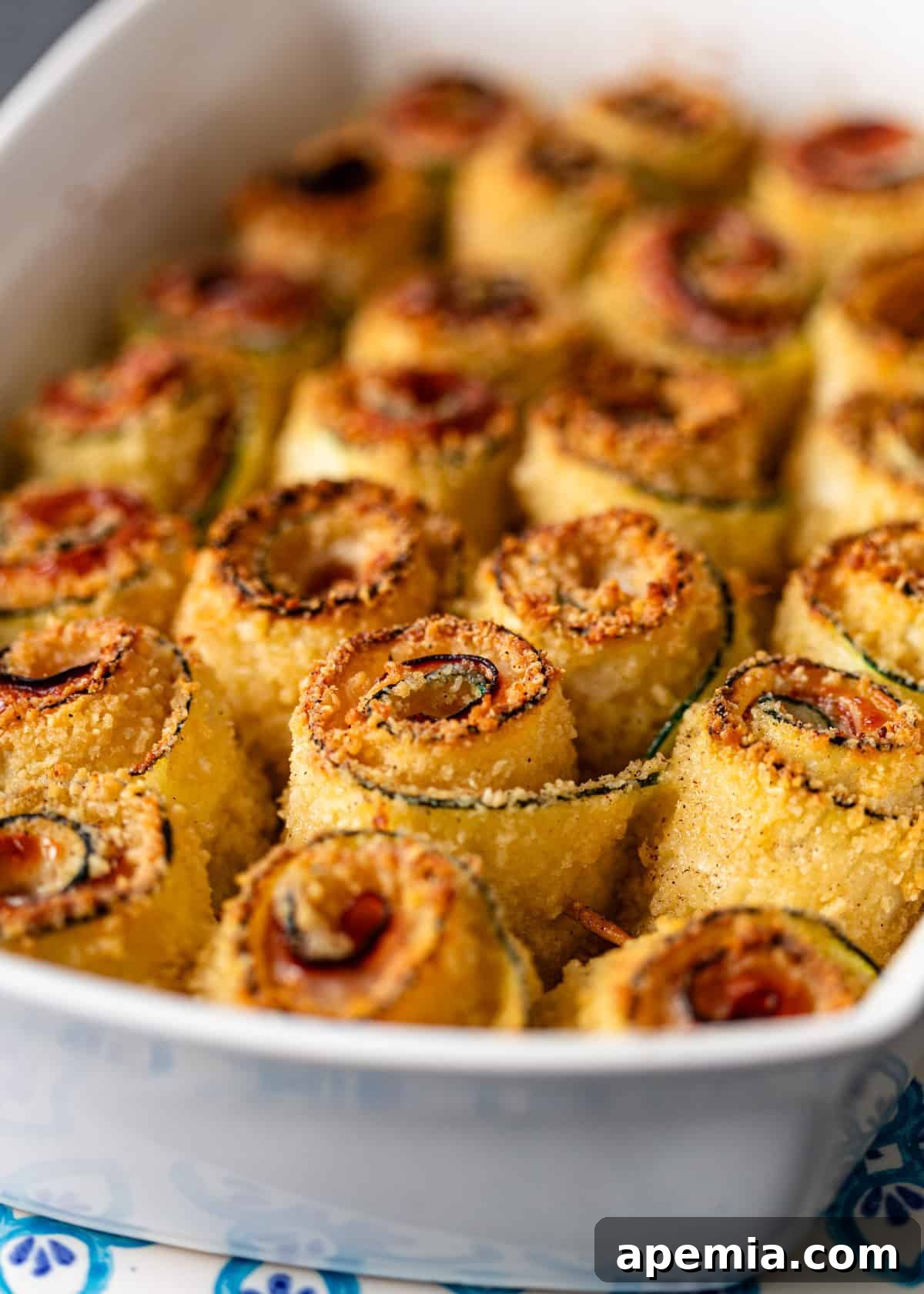 Closeup of crispy zucchini rolls, baked to a golden brown perfection, arranged in a baking dish after being removed from the oven.