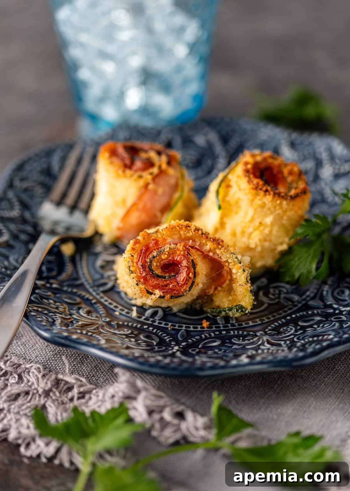 Closeup of a single serving of Crispy Zucchini Involtini on a blue ceramic plate, showcasing the golden crust and melted filling.