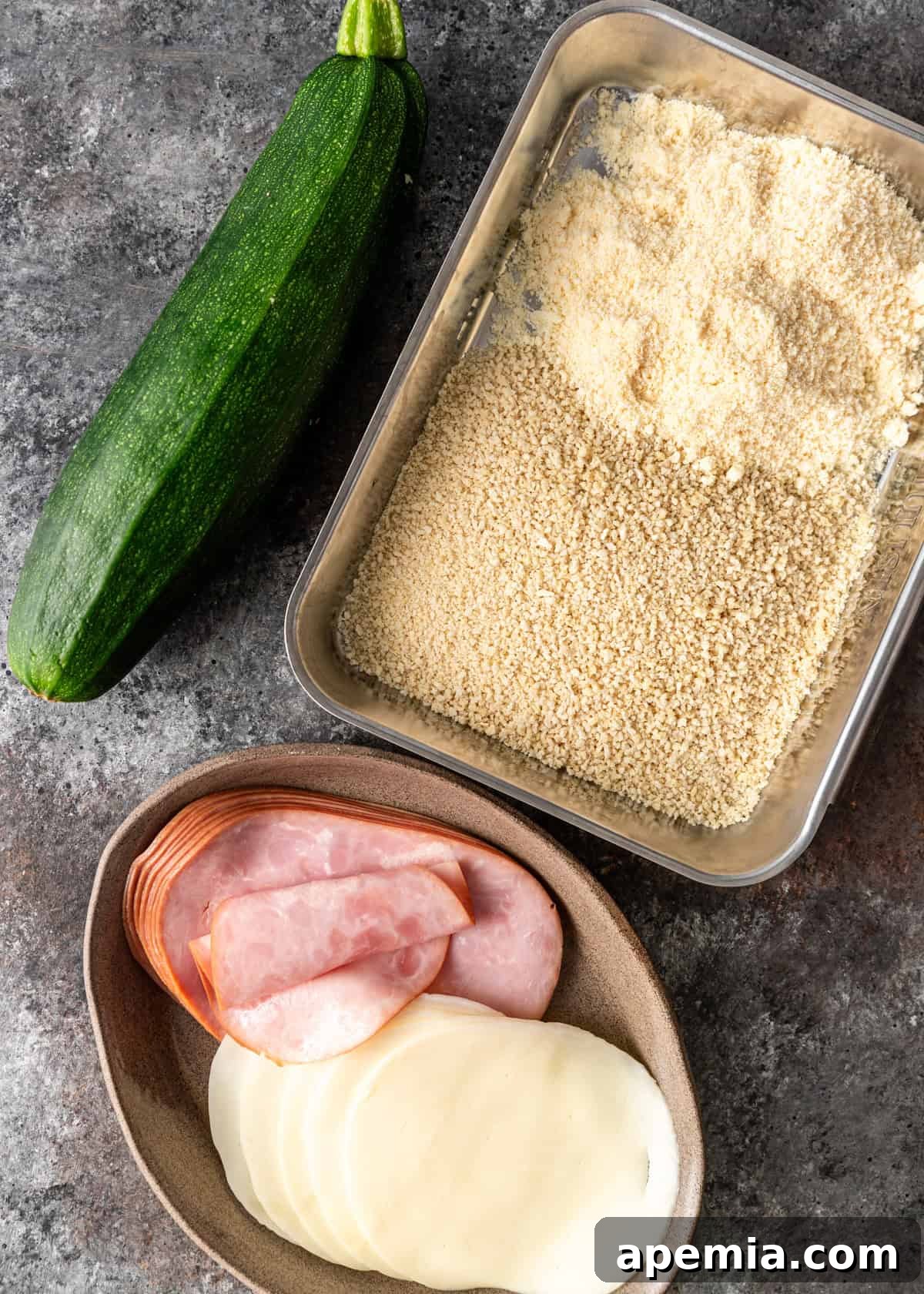 Overhead shot showcasing all the fresh ingredients needed for making Zucchini Involtini, including zucchini, prosciutto, provolone, breadcrumbs, and Parmesan.