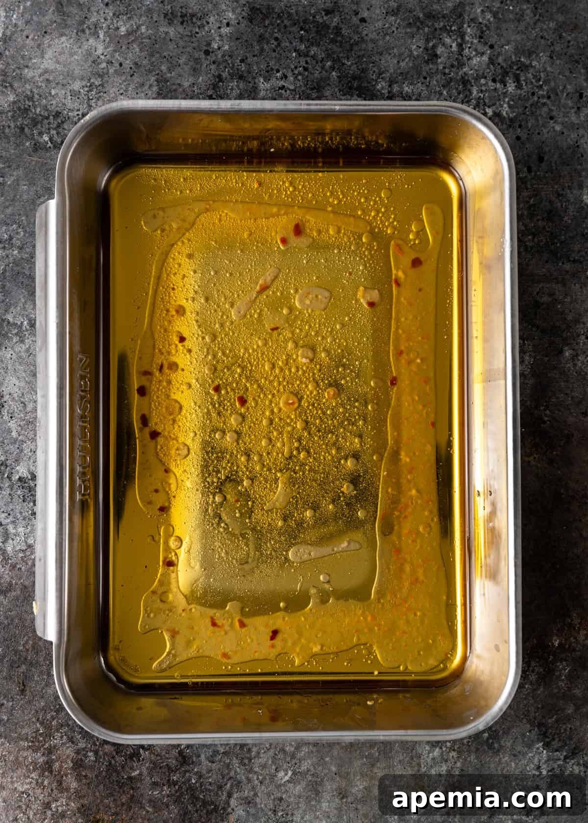 Overhead view of a shallow baking dish containing a pool of olive oil, ready for dipping zucchini ribbons.