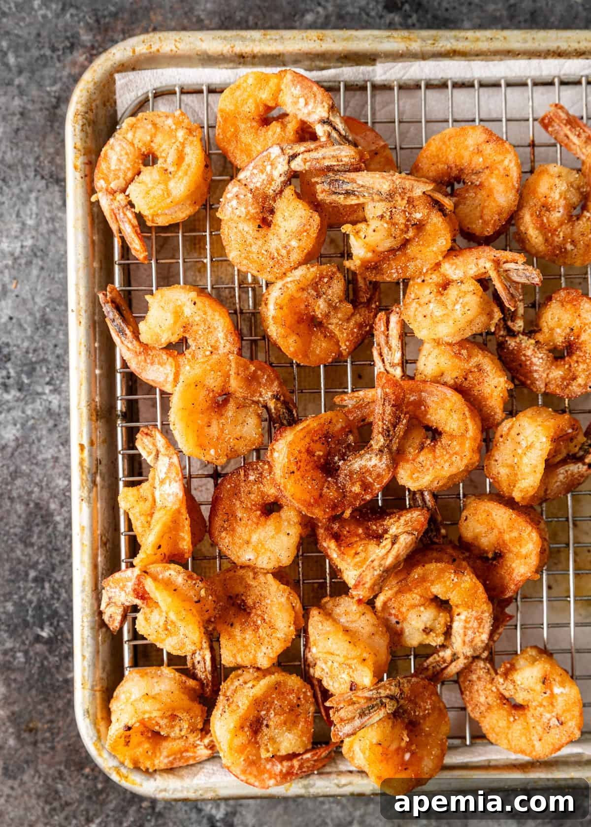 overhead: salt and pepper shrimp cooling on a wire rack over a baking sheet