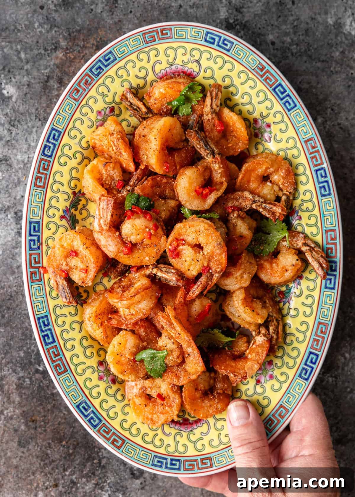 overhead: a hand holding an oval shaped ceramic serving dish full of salt and pepper shrimp stir fry
