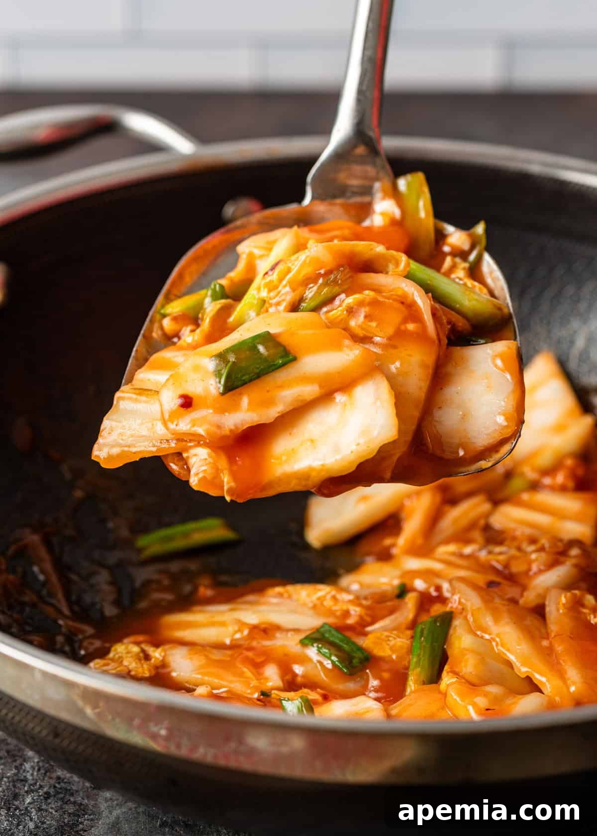 Close-up of a large serving spoon lifting a generous portion of the steaming hot and sour cabbage stir fry from a hot wok, showcasing its glossy sauce and tender vegetables.
