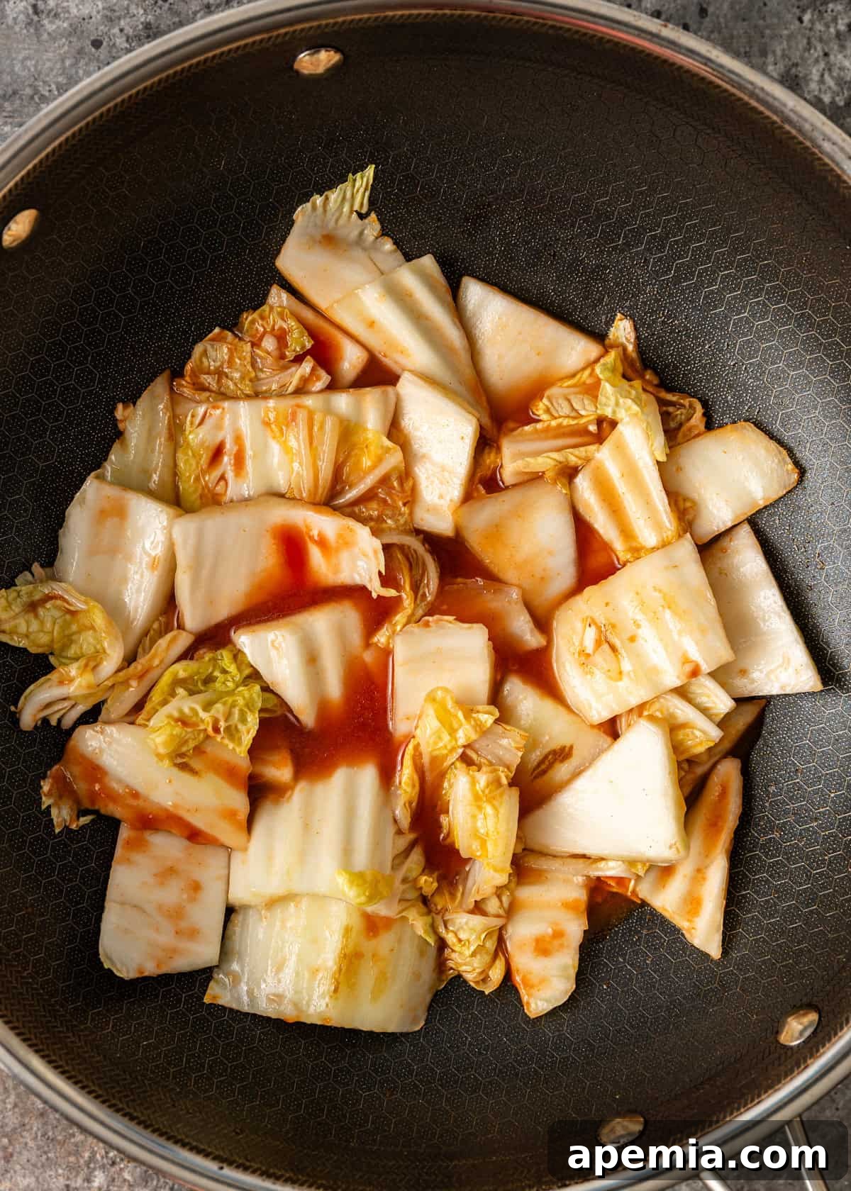 Overhead process shot demonstrating cabbage cooking with rich, glossy sauces in a searing hot wok, capturing the vibrant colors and steam.