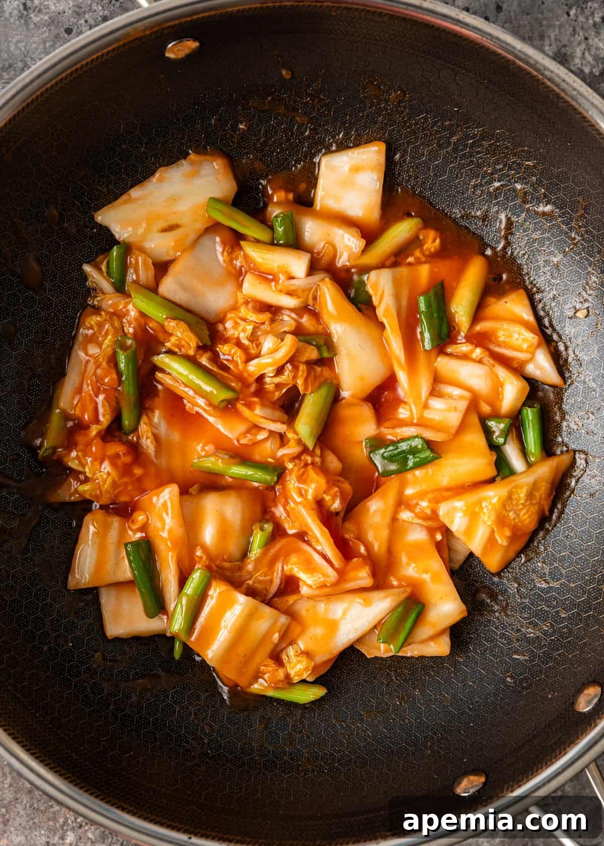Overhead process shot showing hot and sour cabbage stir fry actively cooking in a large wok, with vegetables perfectly coated in sauce and steaming.