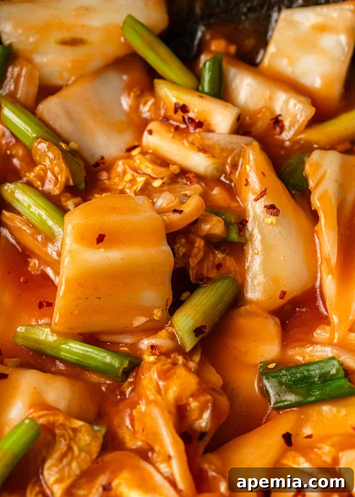 Extreme close-up of the finished hot and sour cabbage stir fry, garnished generously with fresh green onion slices and vibrant red pepper flakes, ready to be served.