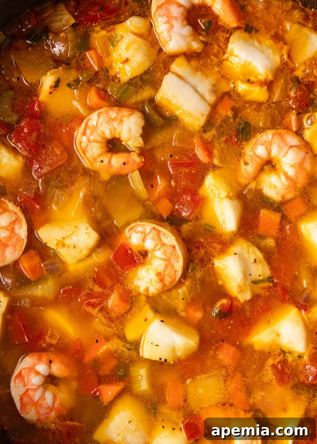 Hearty Greek Fish Stew 11 Extreme close-up of a portion of Greek fish stew, showcasing shrimp, potatoes, carrots, and tomatoes in a rich broth.