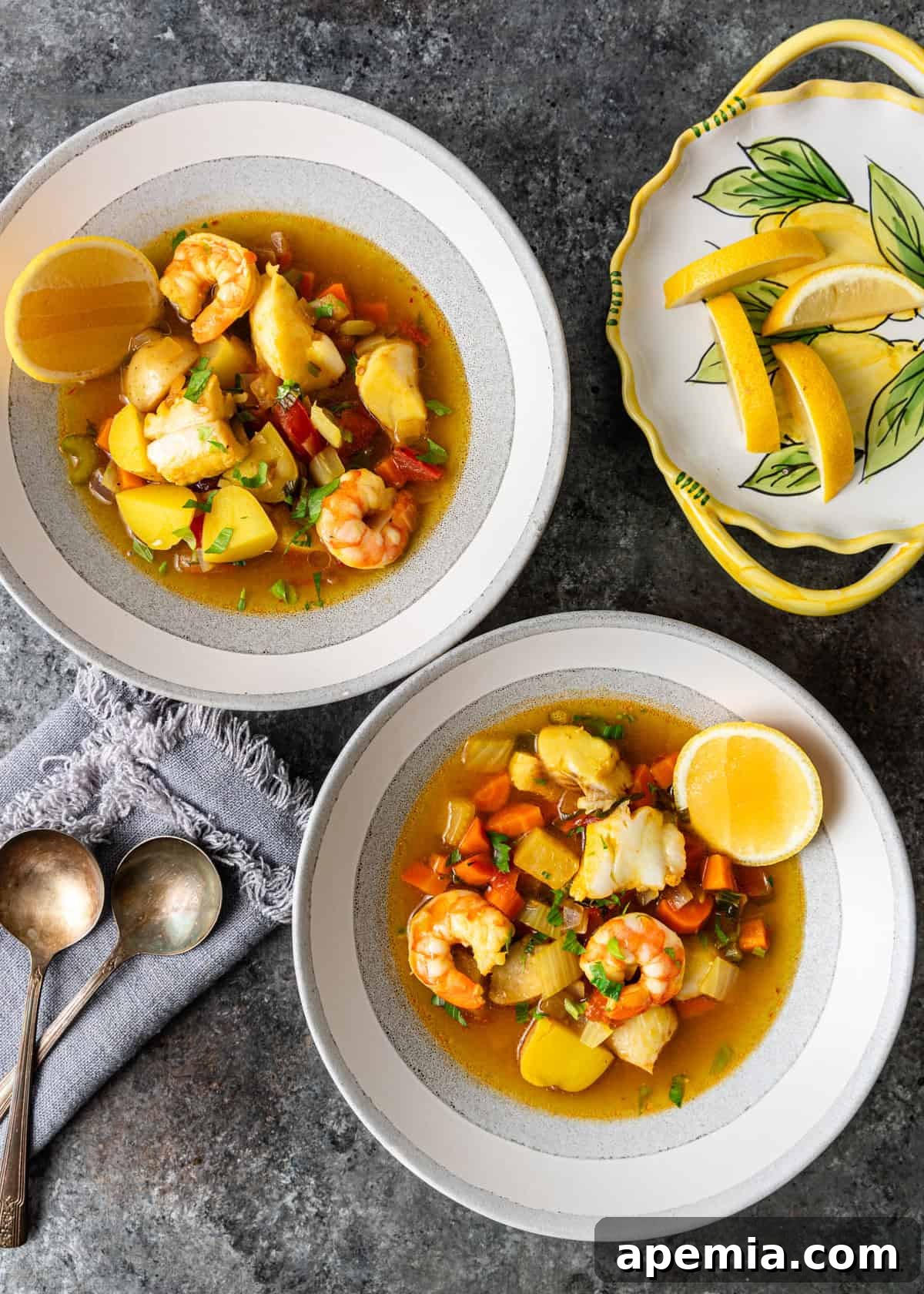 Hearty Greek Fish Stew 12 Overhead view of two bowls of Greek fish stew, each perfectly garnished with lemon wedges, alongside a plate of additional citrus.