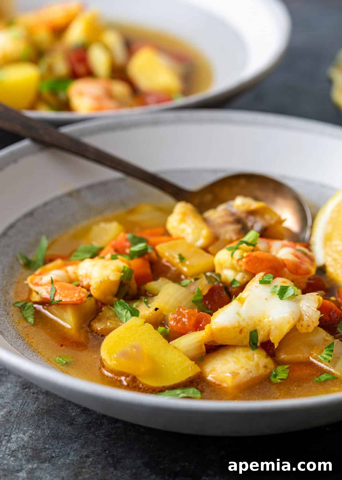 Hearty Greek Fish Stew 13 Close-up side view of a bowl of Greek fish stew with a spoon, showing the rich texture and variety of ingredients.