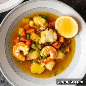 A vibrant bowl of Greek Fish Stew, prepared with fresh ingredients and an aromatic broth, garnished with a slice of lemon.