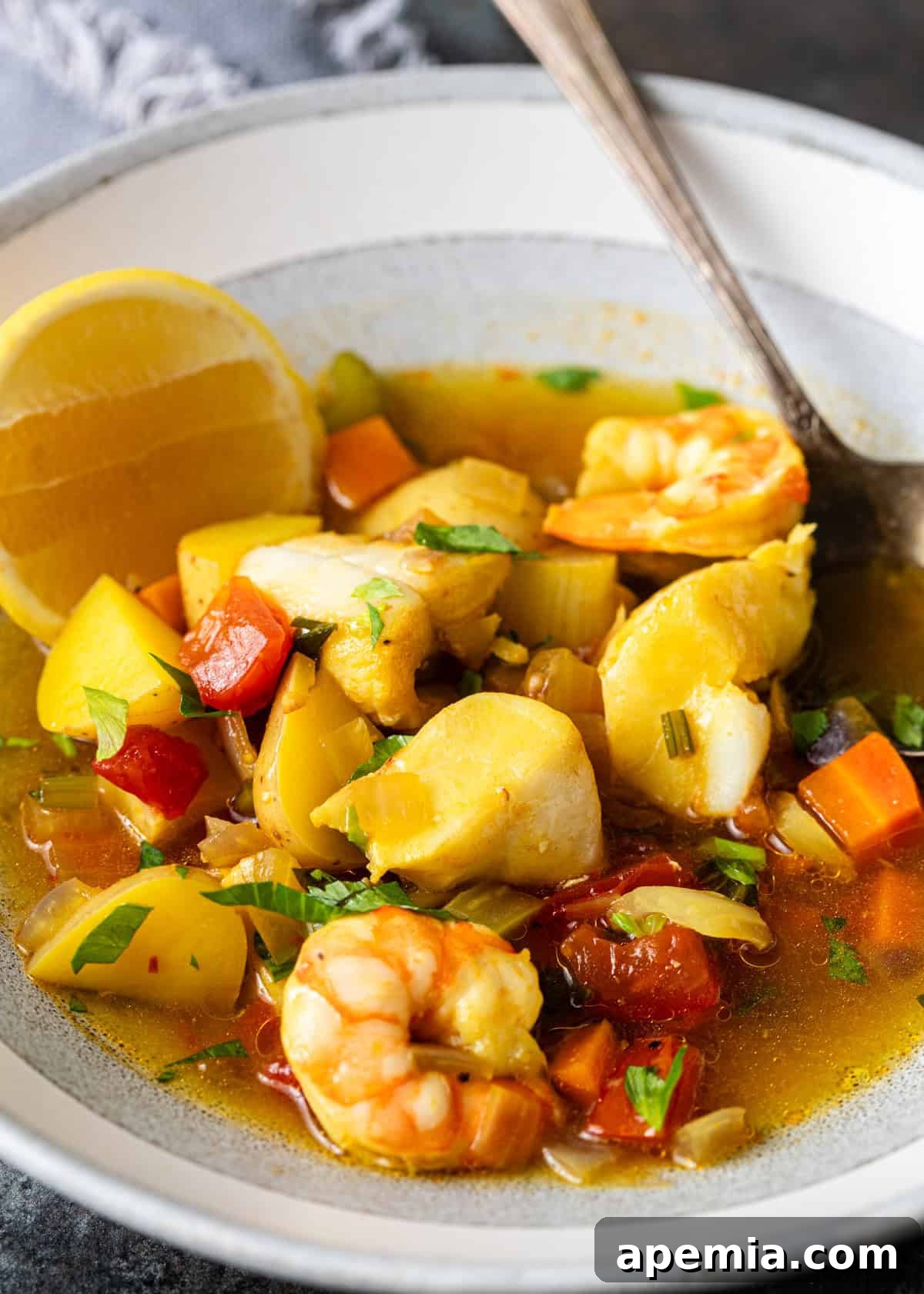 Hearty Greek Fish Stew 3 Close-up view of Greek fish stew, highlighting chunks of fish, shrimp, potatoes, carrots, and vibrant tomatoes.