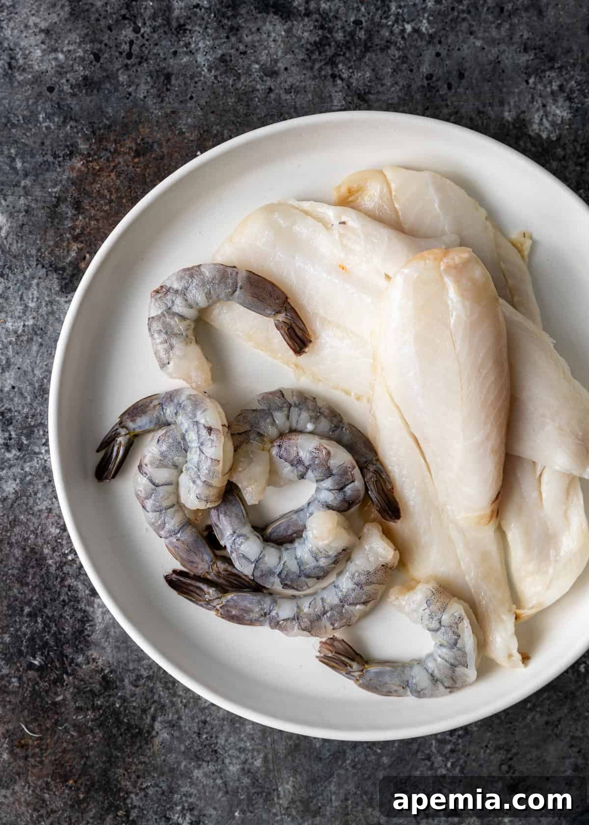Hearty Greek Fish Stew 4 Overhead shot of fresh raw white fish fillets and uncooked shrimp on a plate, ready for preparation.