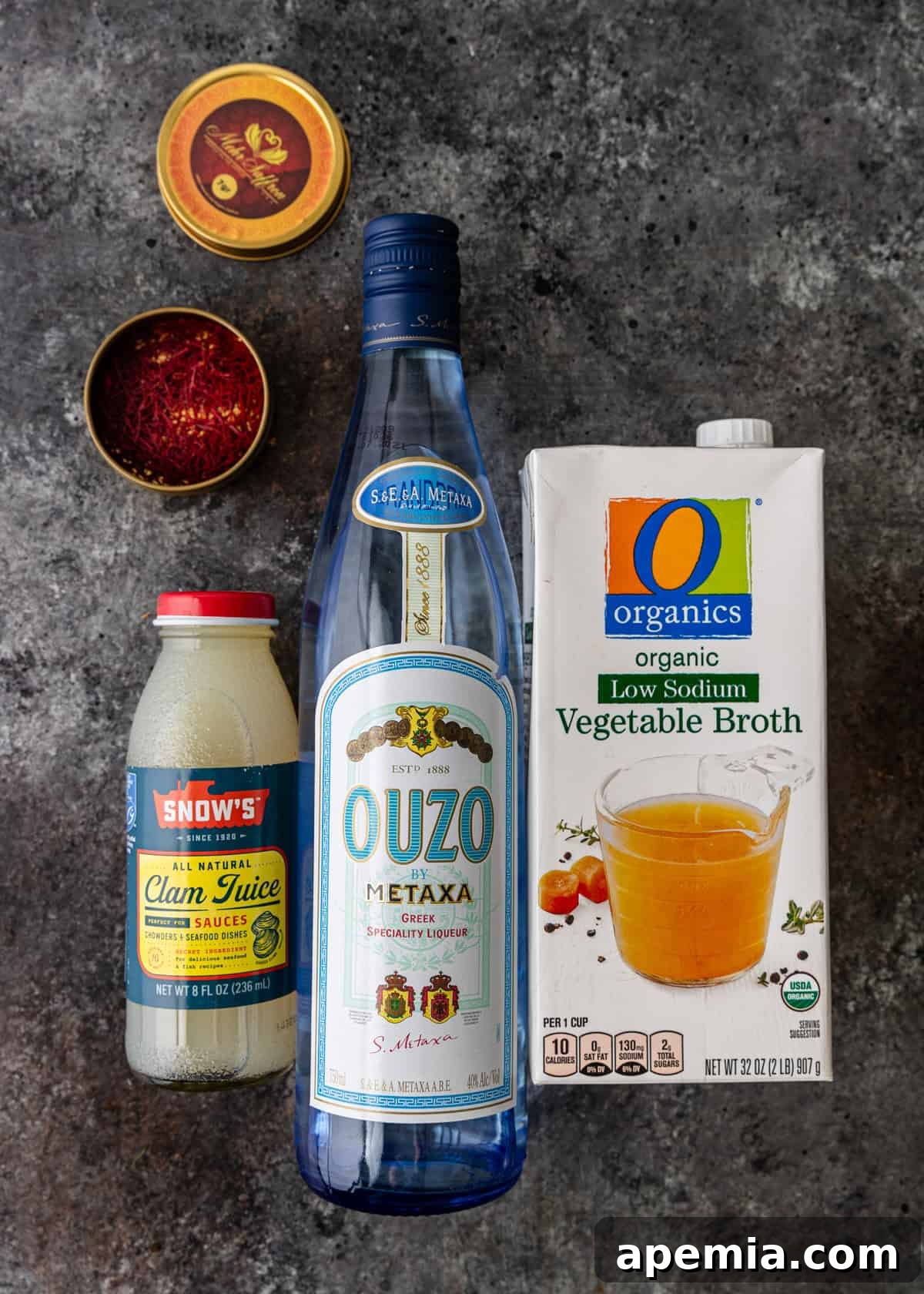 Hearty Greek Fish Stew 6 Ingredients like clam juice, a bottle of ouzo, vegetable broth, and saffron threads are neatly arranged on a kitchen counter.