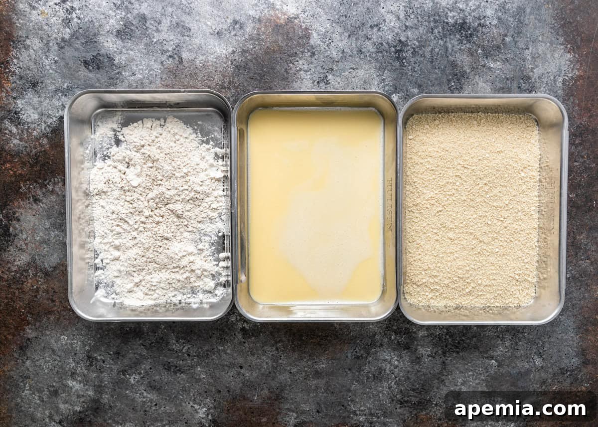 An overhead view of three shallow dishes, perfectly set up as dredging stations for preparing my crispy chicken Milanese recipe, with flour, egg wash, and breadcrumbs.