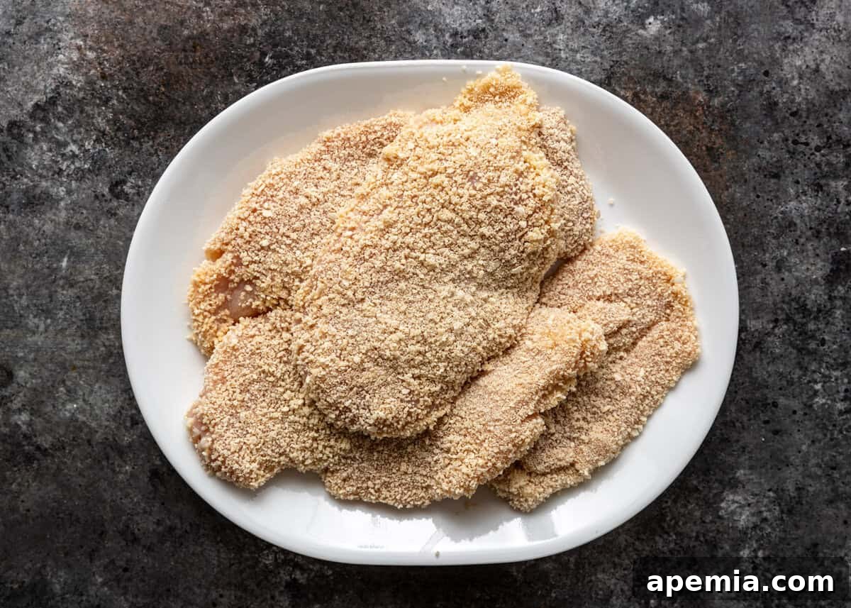 A close-up, overhead shot of several chicken cutlets perfectly coated in seasoned breadcrumbs, ready for frying to create delicious milanesa de pollo.