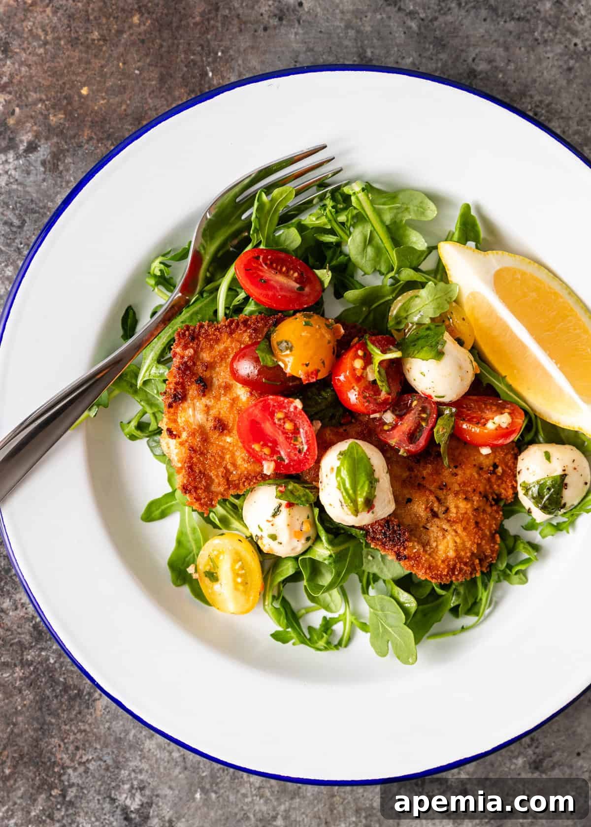 A close-up shot of a crispy milanesa de pollo cutlet nestled over a bed of fresh arugula, topped generously with a vibrant mozzarella and tomato salad, creating a beautiful and flavorful presentation.