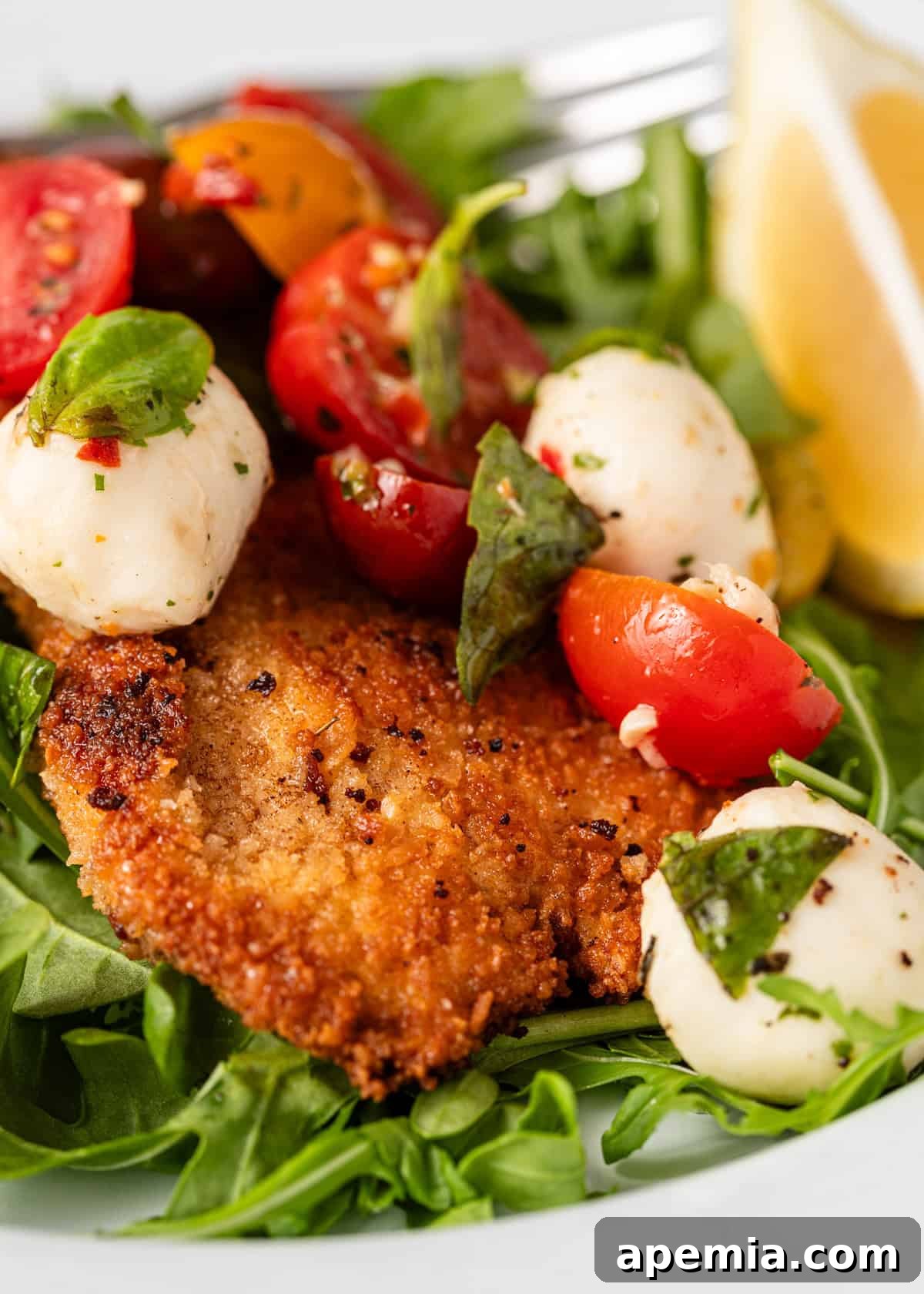 A mouth-watering close-up of a breaded milanesa de pollo cutlet, artfully topped with fresh mozzarella, vibrant basil, and ripe cherry tomatoes, highlighting its irresistible appeal.