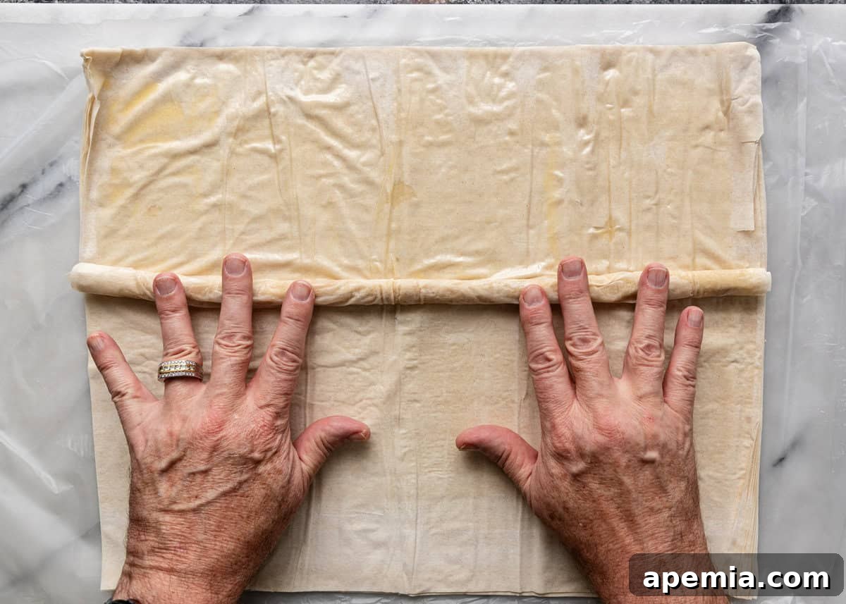 Mhencha: Moroccan Coiled Almond Delight 10 Overhead process shot: a hand gently rolling the filo dough over the almond mhencha filling, forming a neat cylinder.