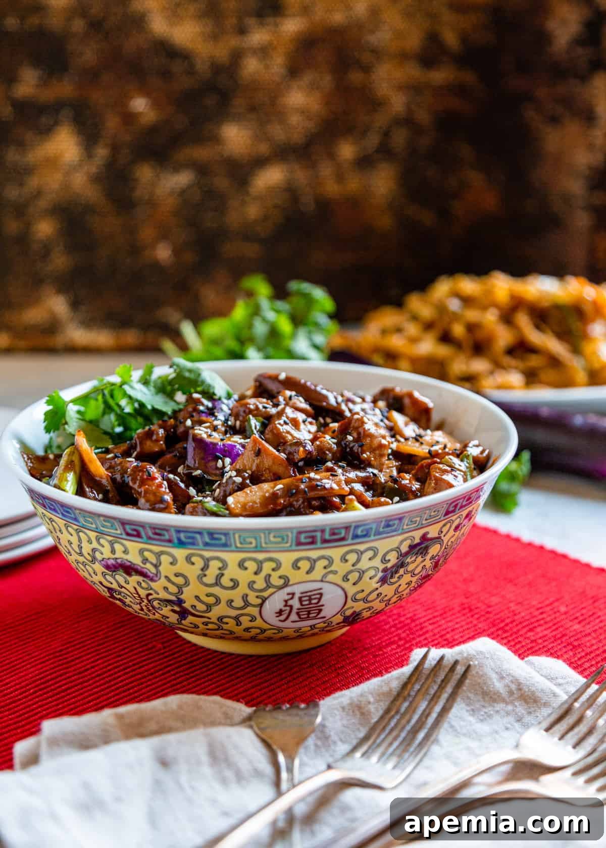 Side view of a beautifully presented Szechuan Pork and Chinese Eggplant Stir Fry in a serving bowl, set on a table with a red placemat and white linen napkin.