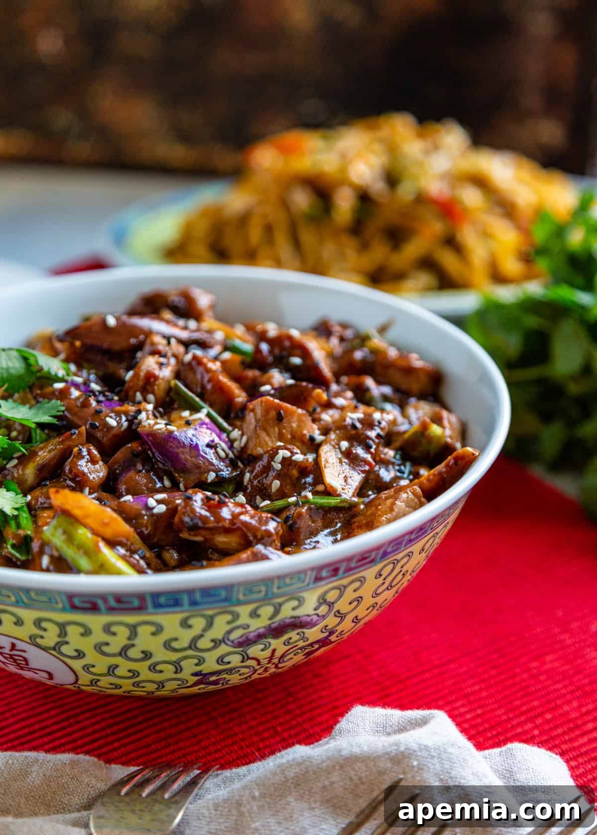 Side view of Szechuan Pork and Chinese Eggplant Stir Fry in a serving bowl, elegantly placed on a red tablecloth with forks resting on a white tea towel.