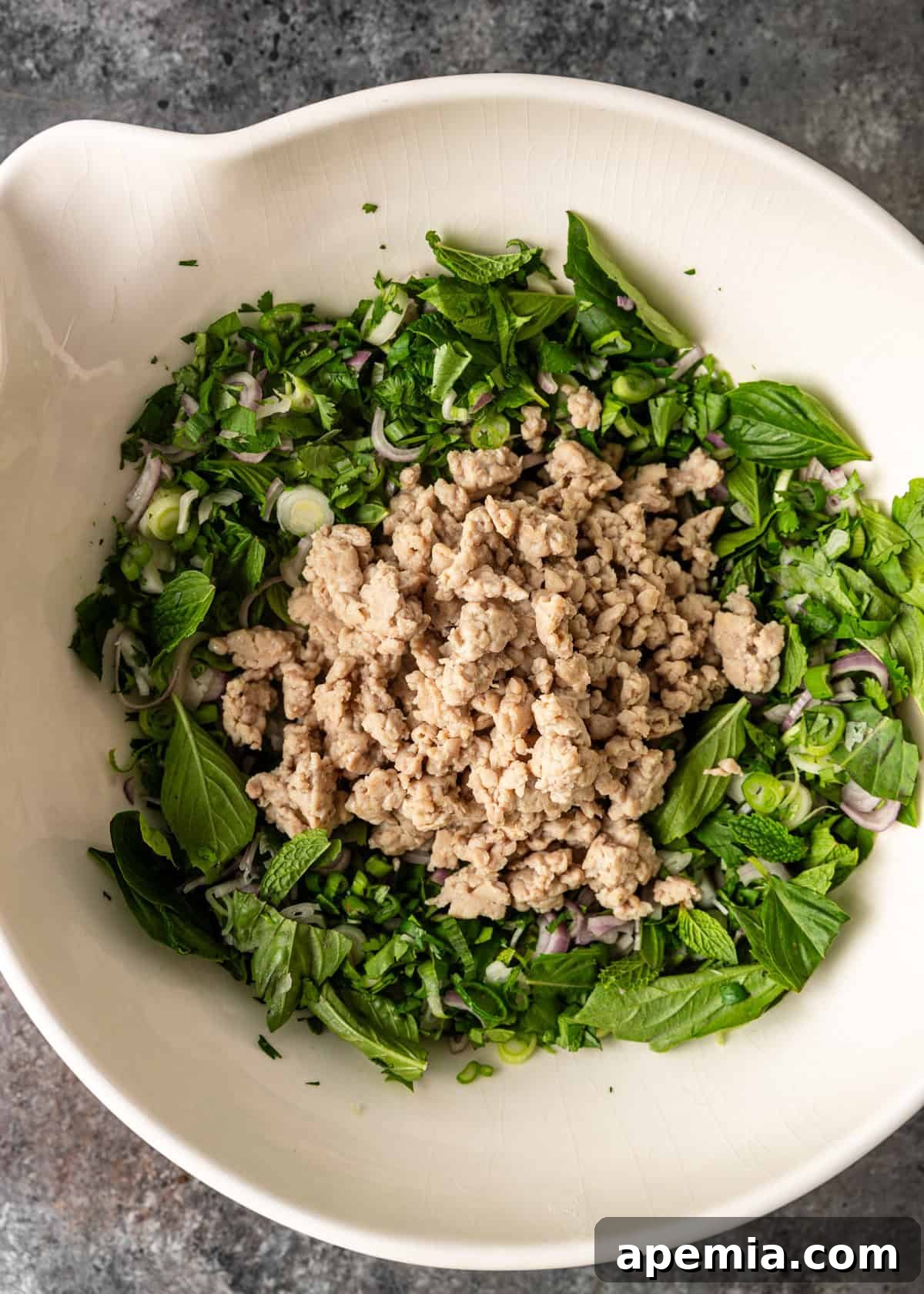 Zesty Thai Larb Gai Chicken Lettuce Wraps 9 overhead process shot: ground chicken in a bowl with herbs and onion before mixing