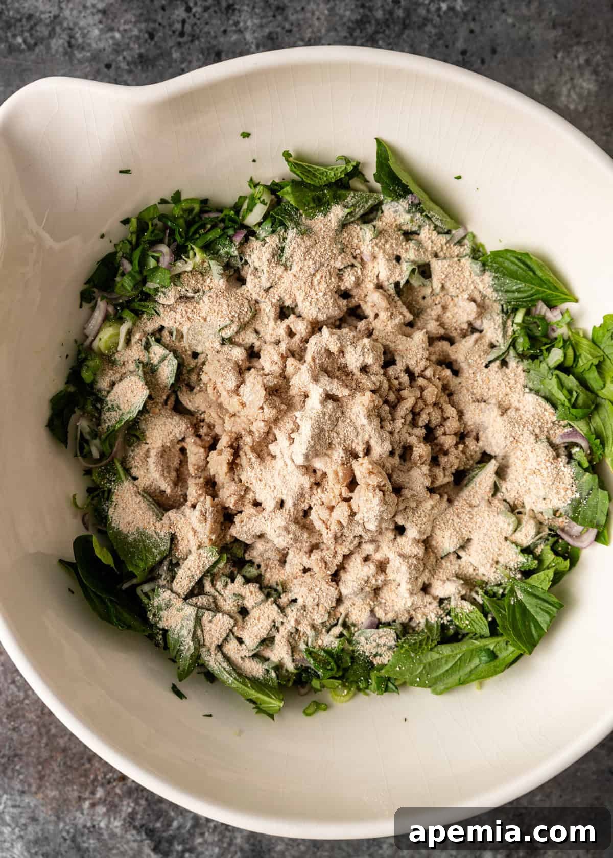 Zesty Thai Larb Gai Chicken Lettuce Wraps 10 overhead process shot: ground chicken in a bowl with herbs, onion, and ground toasted rice before mixing