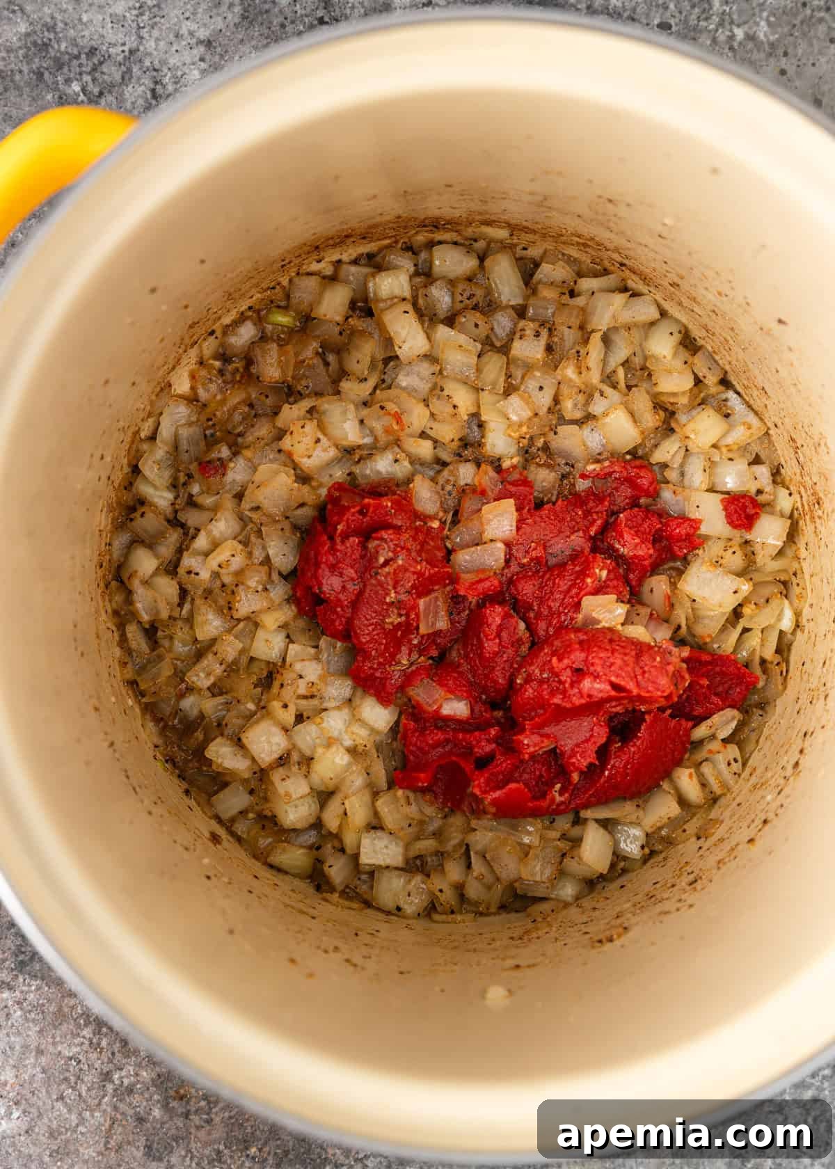 Overhead process shot: adding rich tomato paste to softened onion and garlic in a sturdy pot.