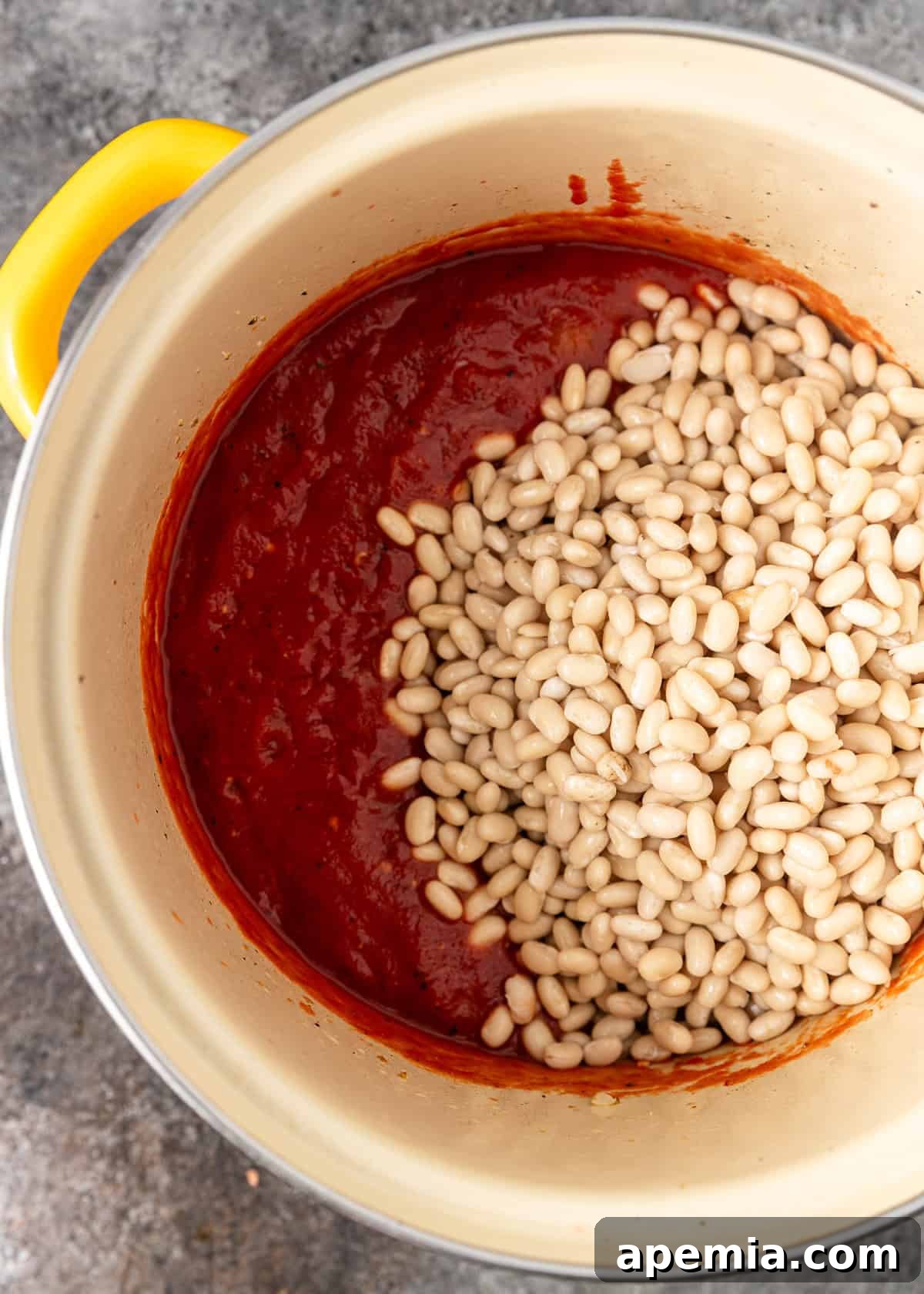 Overhead process shot: adding pre-soaked white beans to the reduced tomato paste and aromatics mixture.