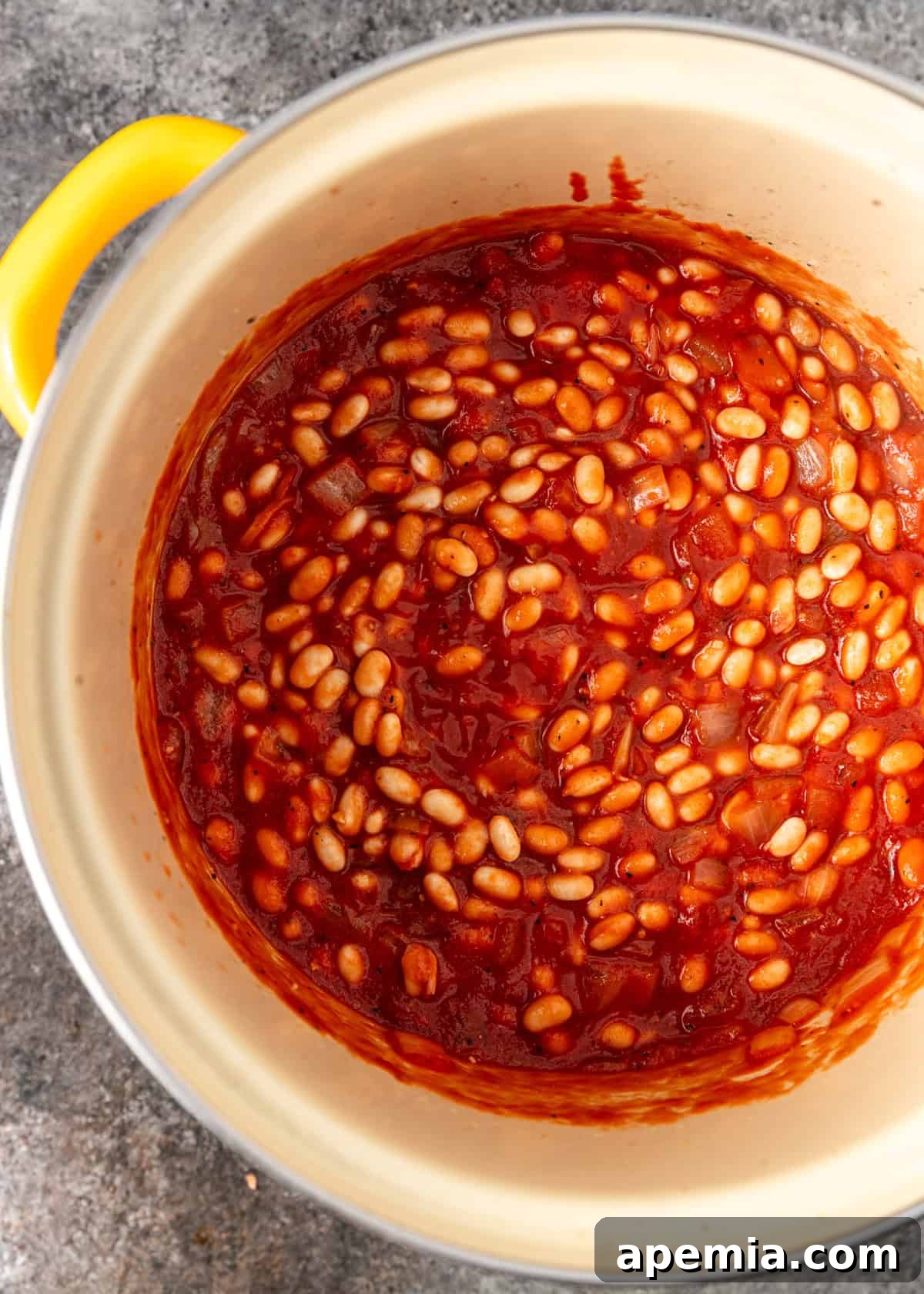 Overhead process shot: A pot of Fasoolia Baida simmering gently, showing the stew's liquid and beans.