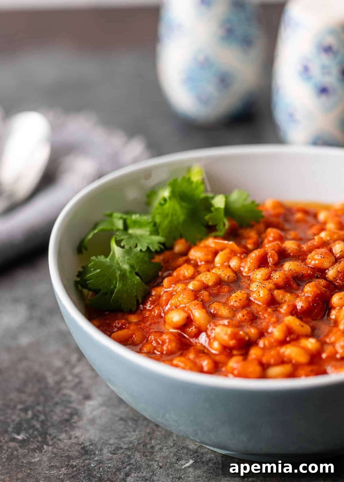 Side view closeup of a serving of white bean stew in a light blue bowl, showing the creamy texture of the beans.