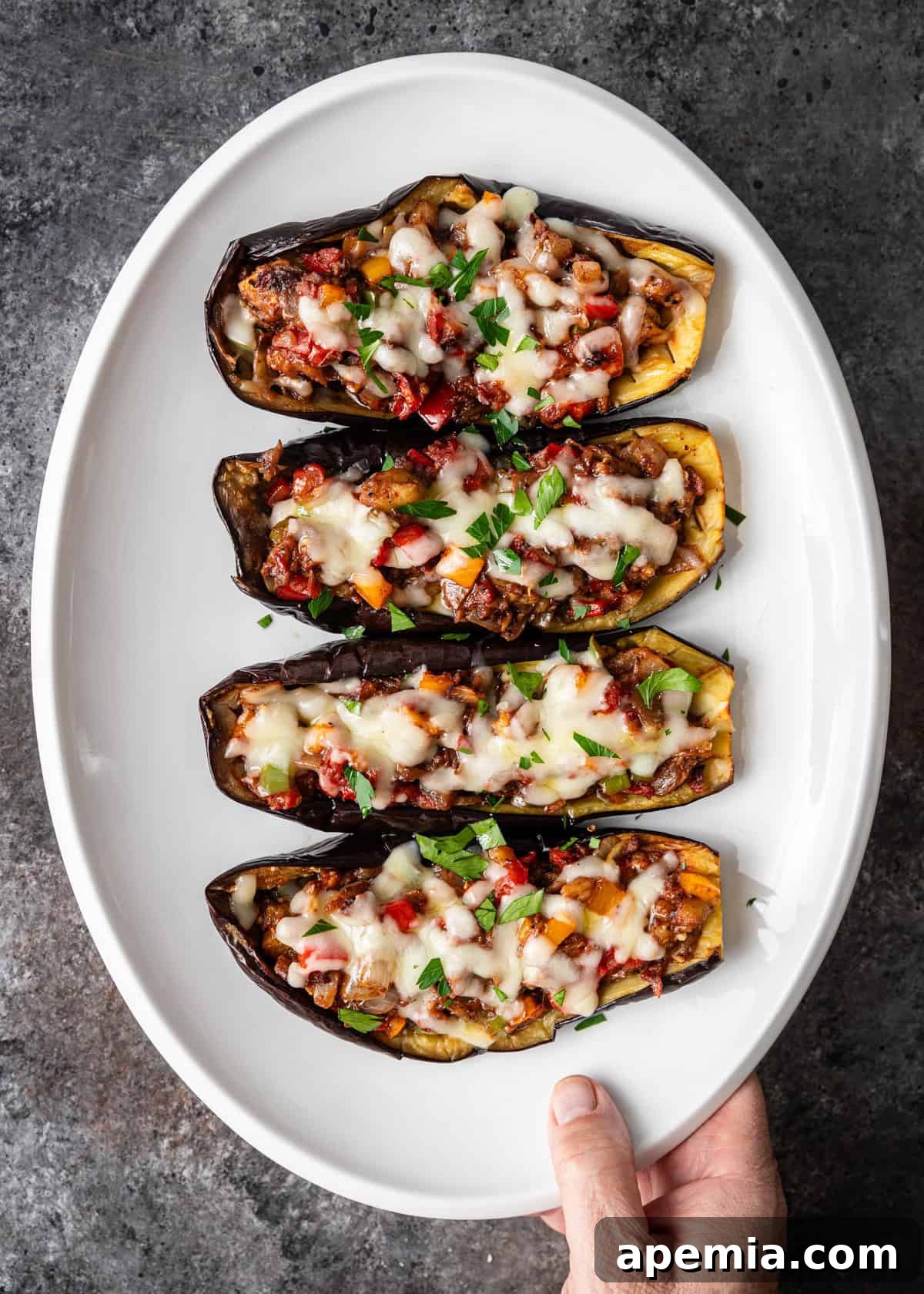 overhead: a hand holding a white platter with 4 stuffed eggplant