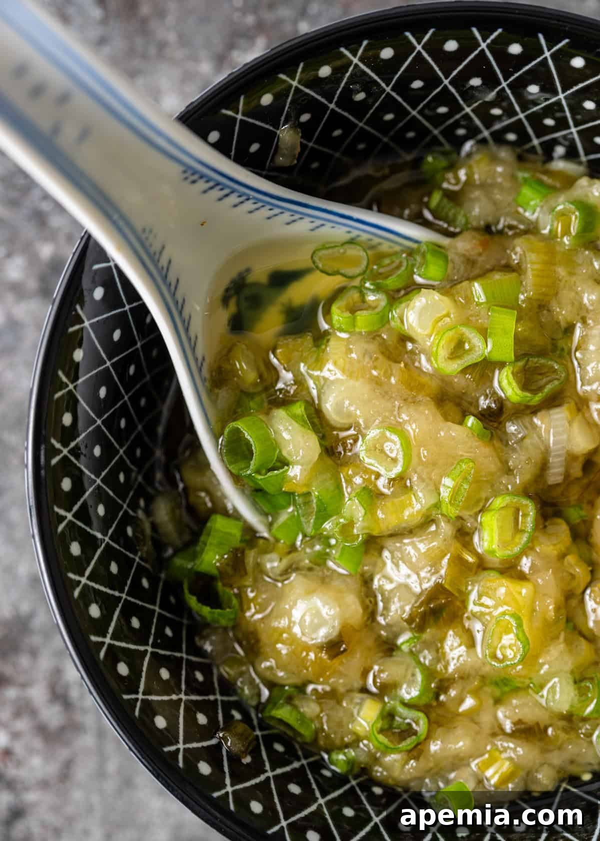 Overhead closeup shot of the vibrant ginger scallion sauce in a small black and white bowl with a large soup spoon