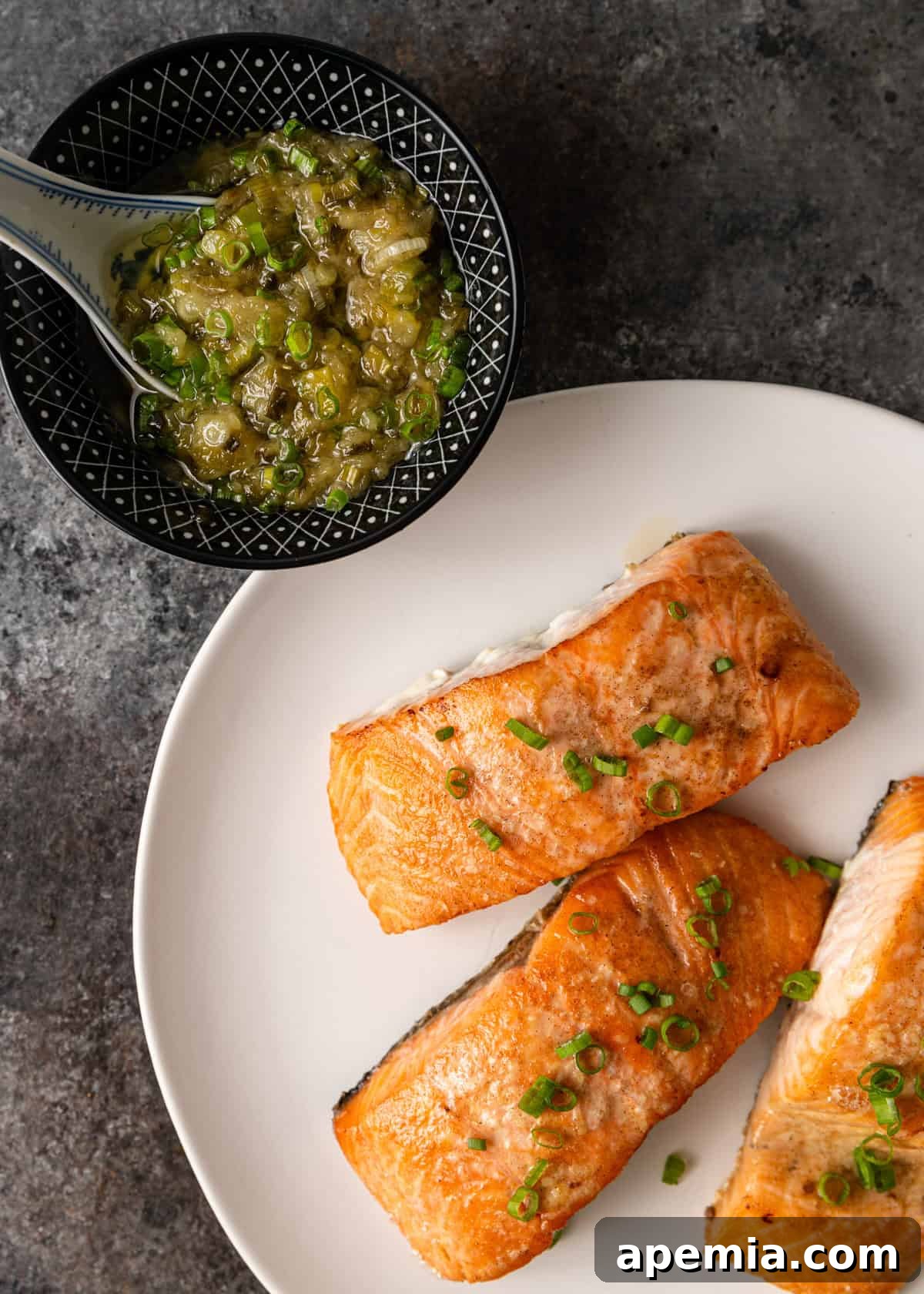 Overhead view of three baked salmon fillets alongside a small bowl of ginger scallion sauce