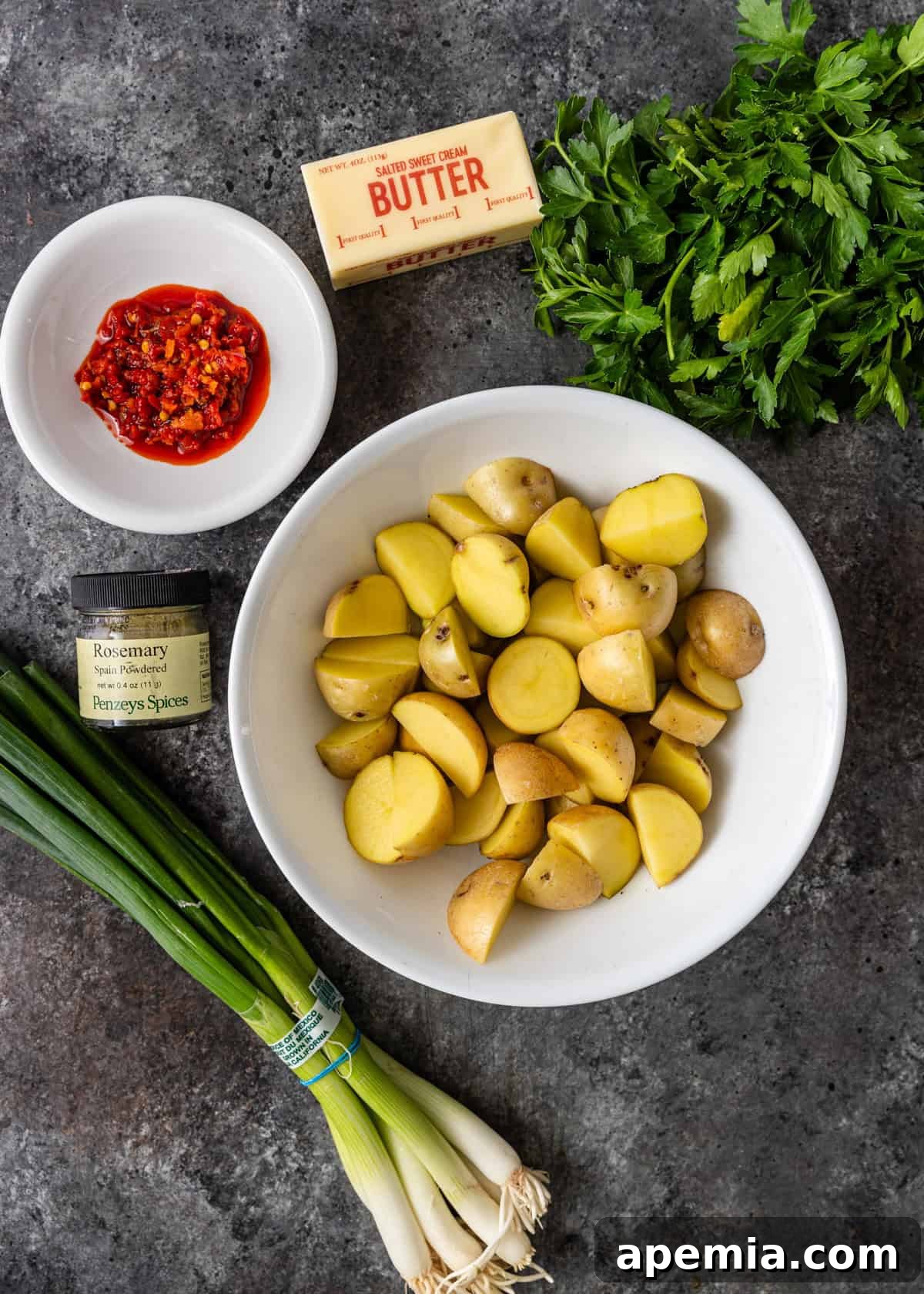 Overhead shot displaying all the fresh ingredients needed to make Calabrian potatoes, arranged neatly in bowls on a kitchen counter.