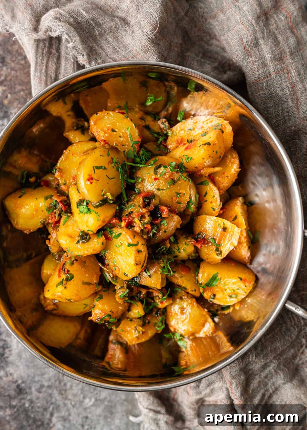 Overhead view of a gleaming metal bowl filled with cooked Calabrian chili potatoes, glistening with herb butter and ready to serve.