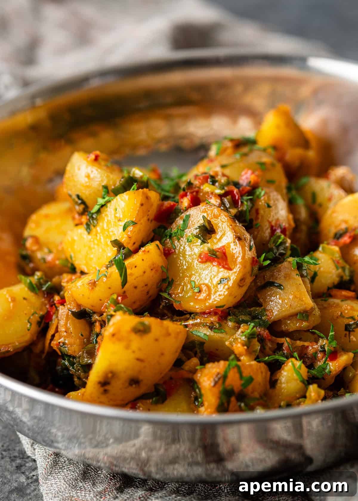 Closeup of Calabrian chili potatoes generously topped with fresh chopped herbs in a metal bowl, emphasizing their appetizing presentation.