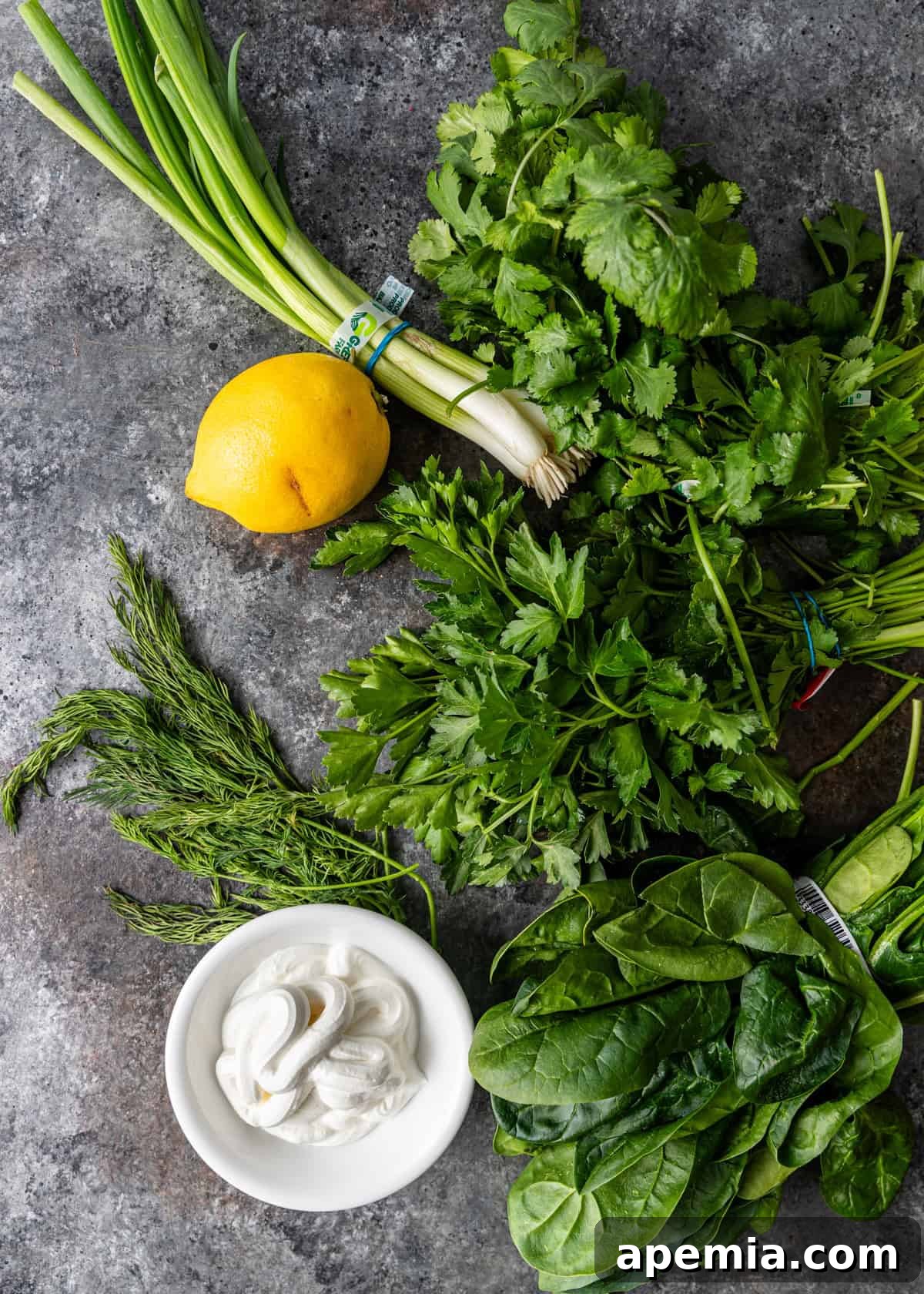 Overhead view of fresh herbs, cheese, lemon, and spinach, key garnishes for Persian Noodle Soup.