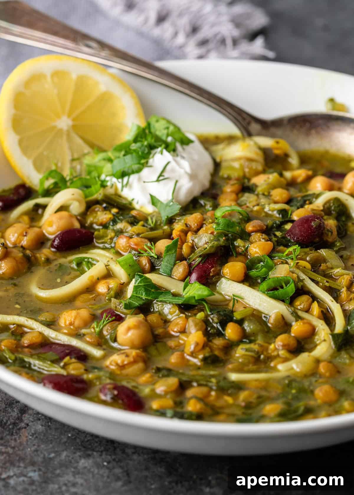 Closeup of Iranian Noodle Soup, highlighting the noodles, beans, and fresh herbs within the broth.