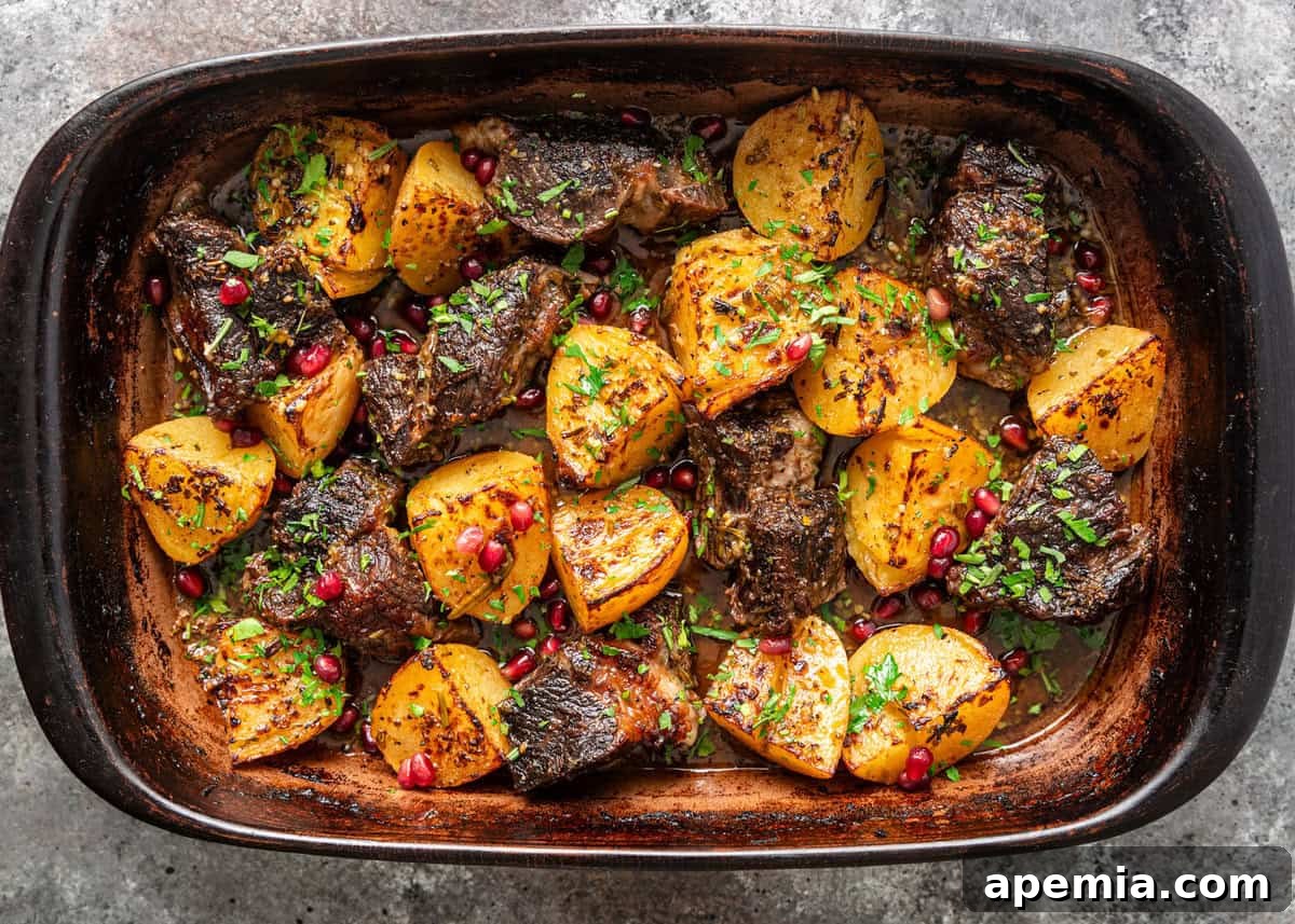 overhead: pot roast with potato wedges and pomegranate arils in a baking dish