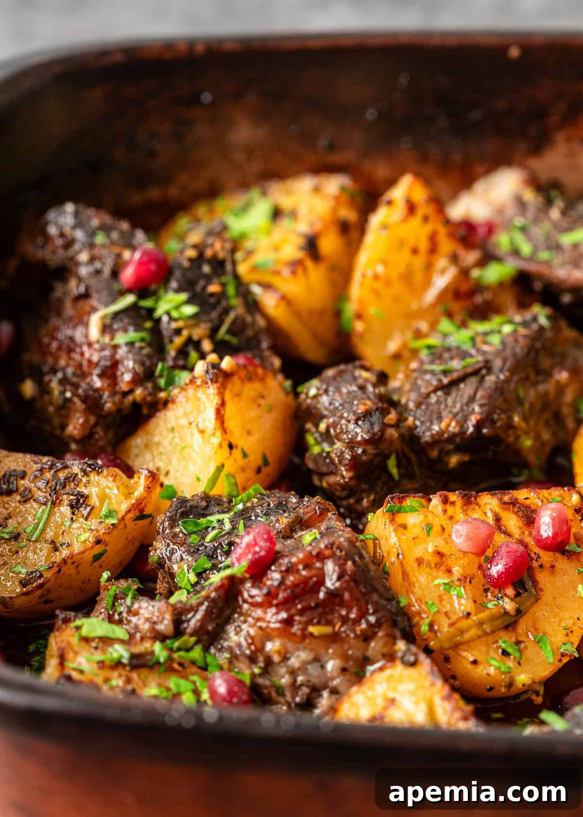 closeup: pot roast in oven with potatoes, herbs, and pomegranate arils