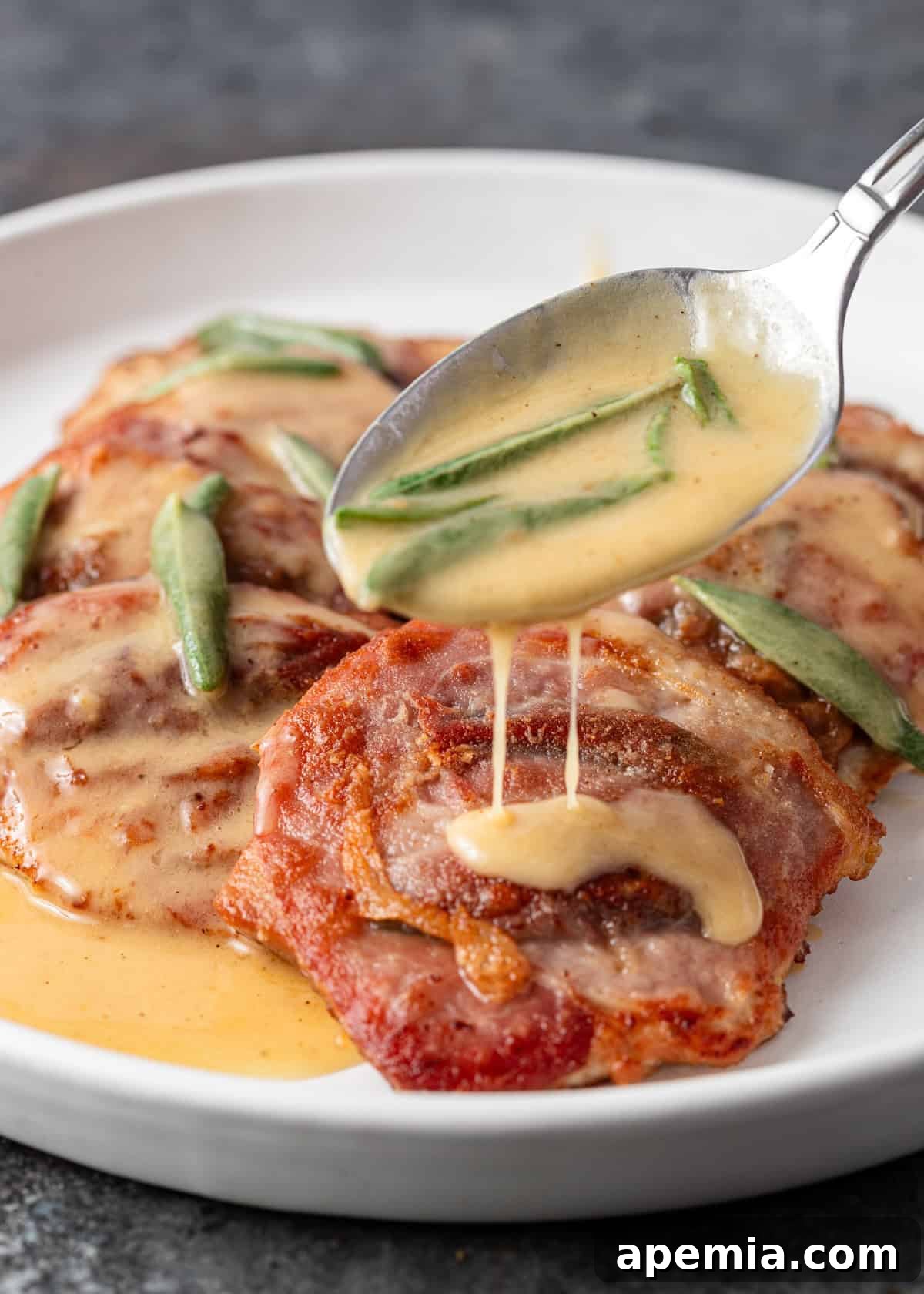 Side view: A hand spooning the glossy sage butter sauce over a perfectly cooked pork saltimbocca cutlet on a plate.