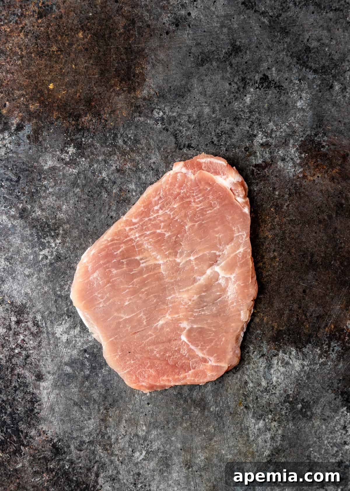 Process shot: A pork cutlet being pounded thinly between plastic wrap.