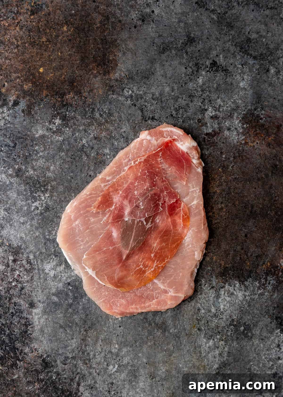 Process shot: Layering slices of prosciutto over the sage leaf on the cutlet.