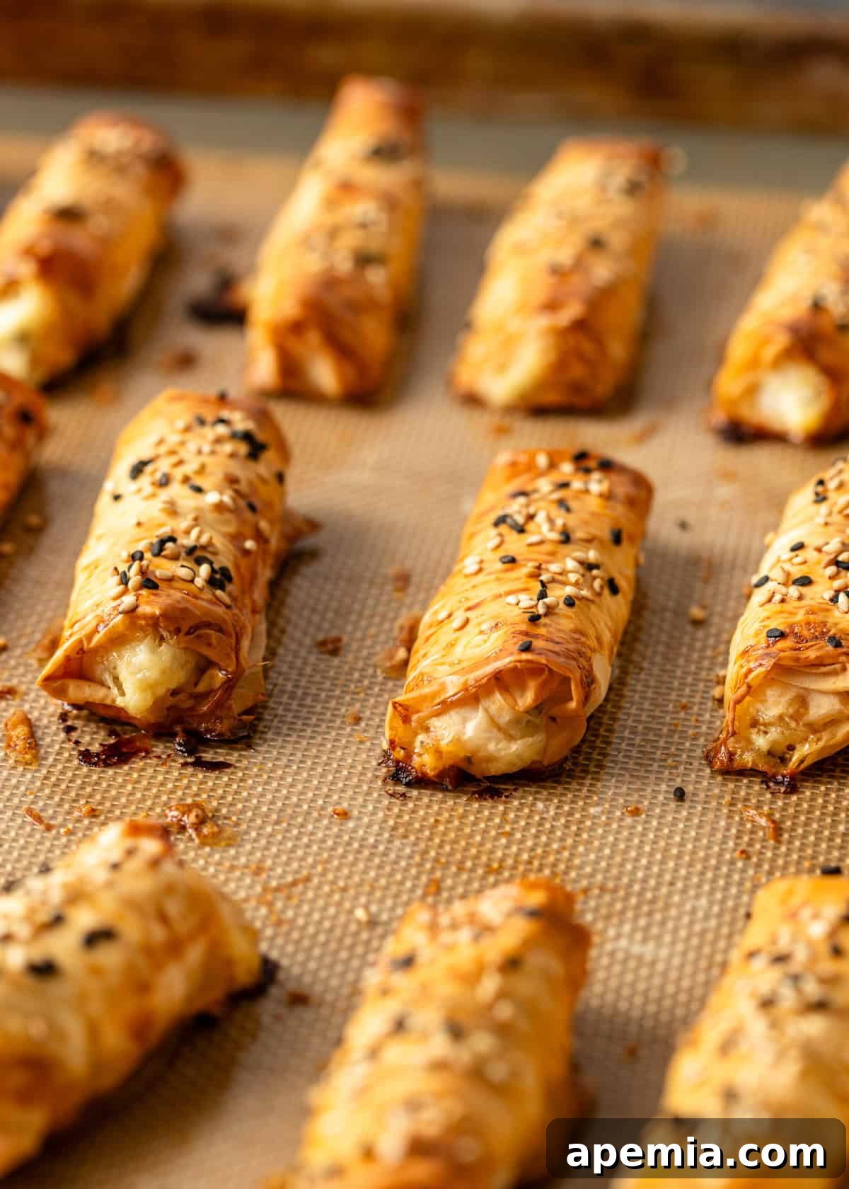 Golden Feta Börek Rolls 3 Closeup: Several unbaked feta pastry cigars neatly arranged on a Silpat baking mat, ready for the oven.