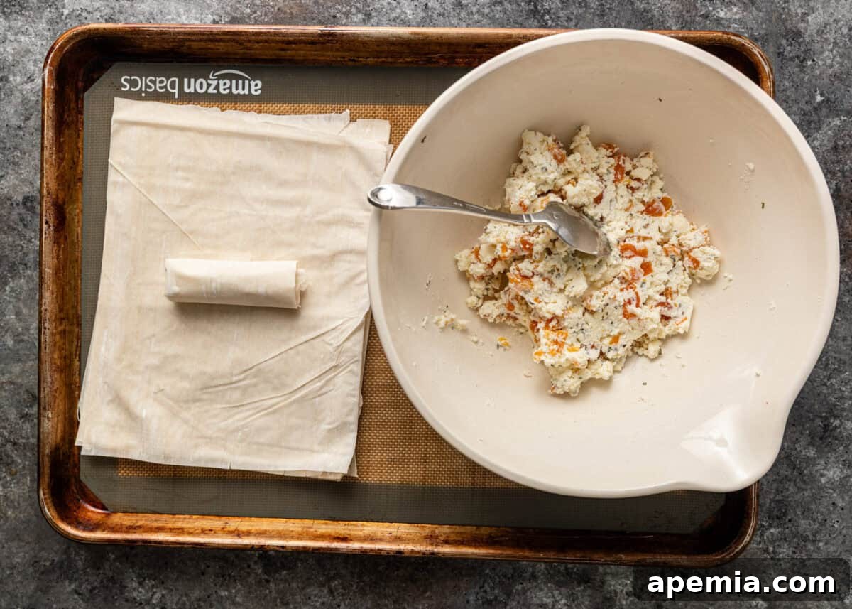 Golden Feta Börek Rolls 8 Overhead process shot: A perfectly rolled phyllo cigar next to a bowl of filling, ready for baking.