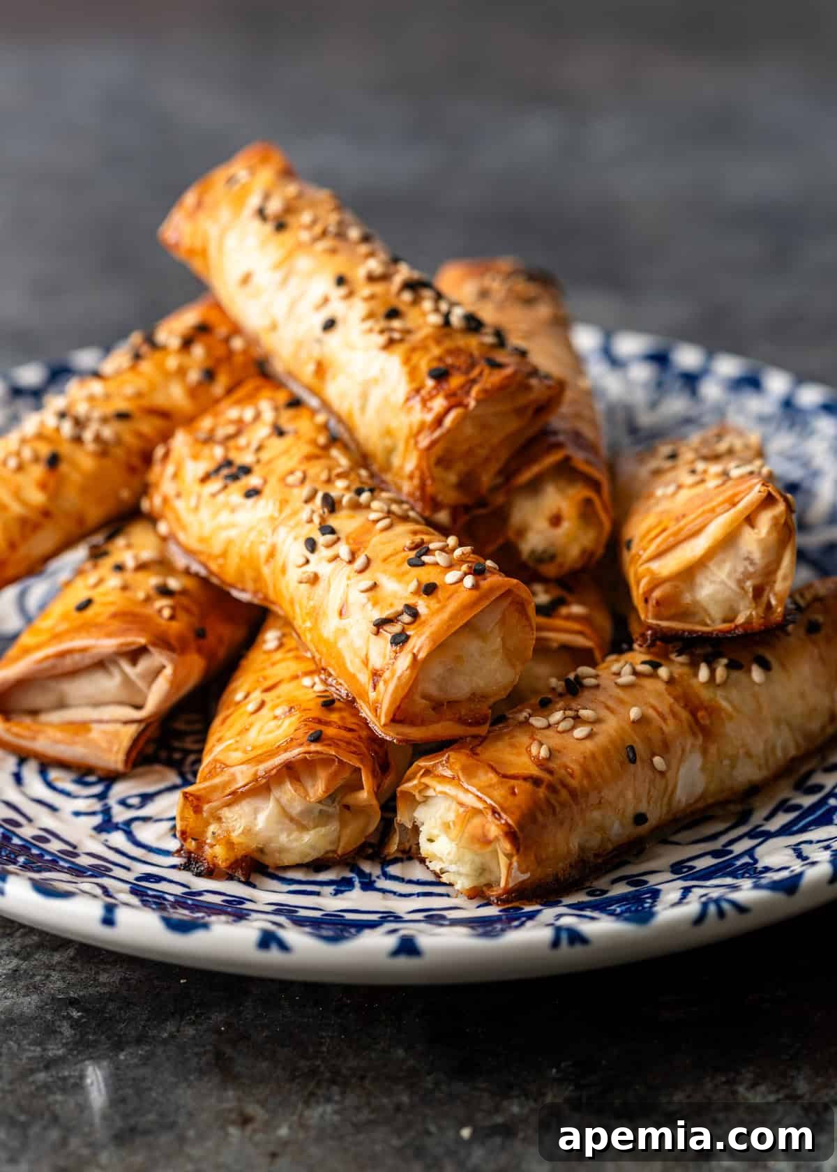 Golden Feta Börek Rolls 10 Closeup: A stack of perfectly baked feta pastry cigars, golden and crispy, on a blue and white patterned plate.