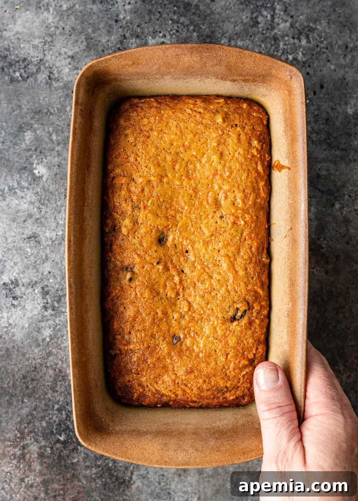 overhead: a hand holding my carrot cake recipe in a loaf pan after baking