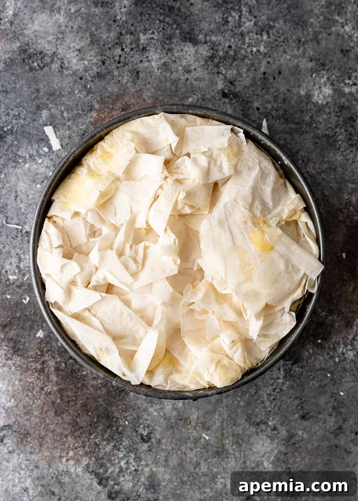Overhead process shot illustrating the top layers of filo sheets being neatly folded over the custard filling in a springform pan.